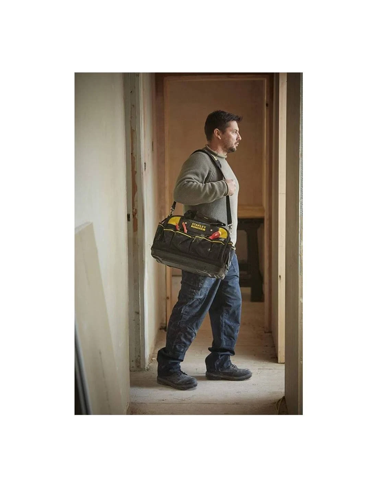 Mężczyzna niesie torbę z narzędziami, idąc przez korytarz.