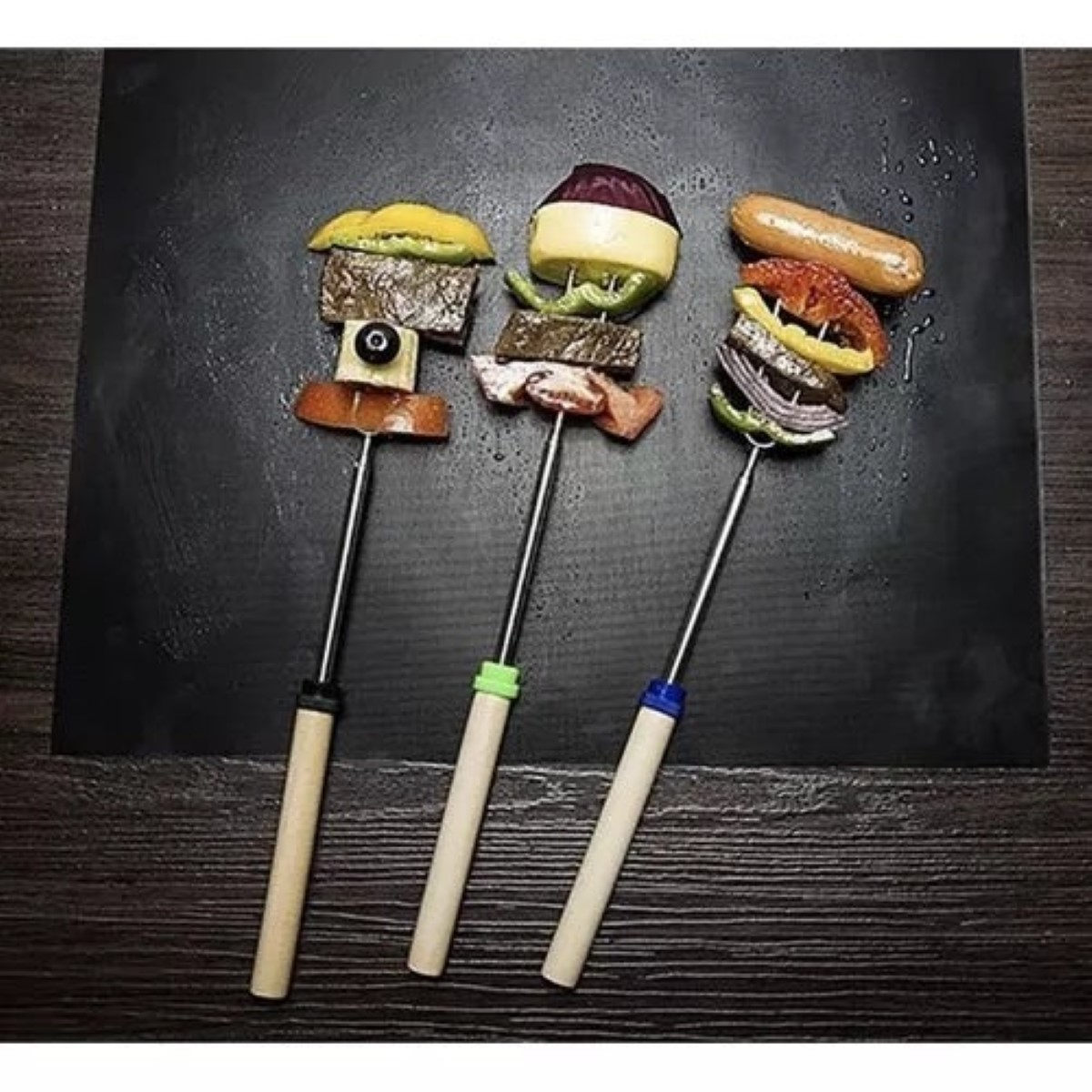 Tres brochetas con comida: carne, verduras, salchicha y queso sobre superficie oscura.