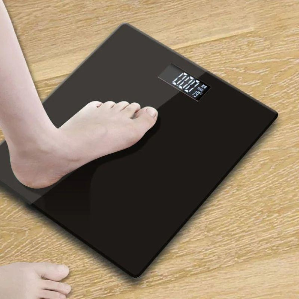 Un pie sobre una báscula negra en suelo de madera. Pantalla digital 0.00.