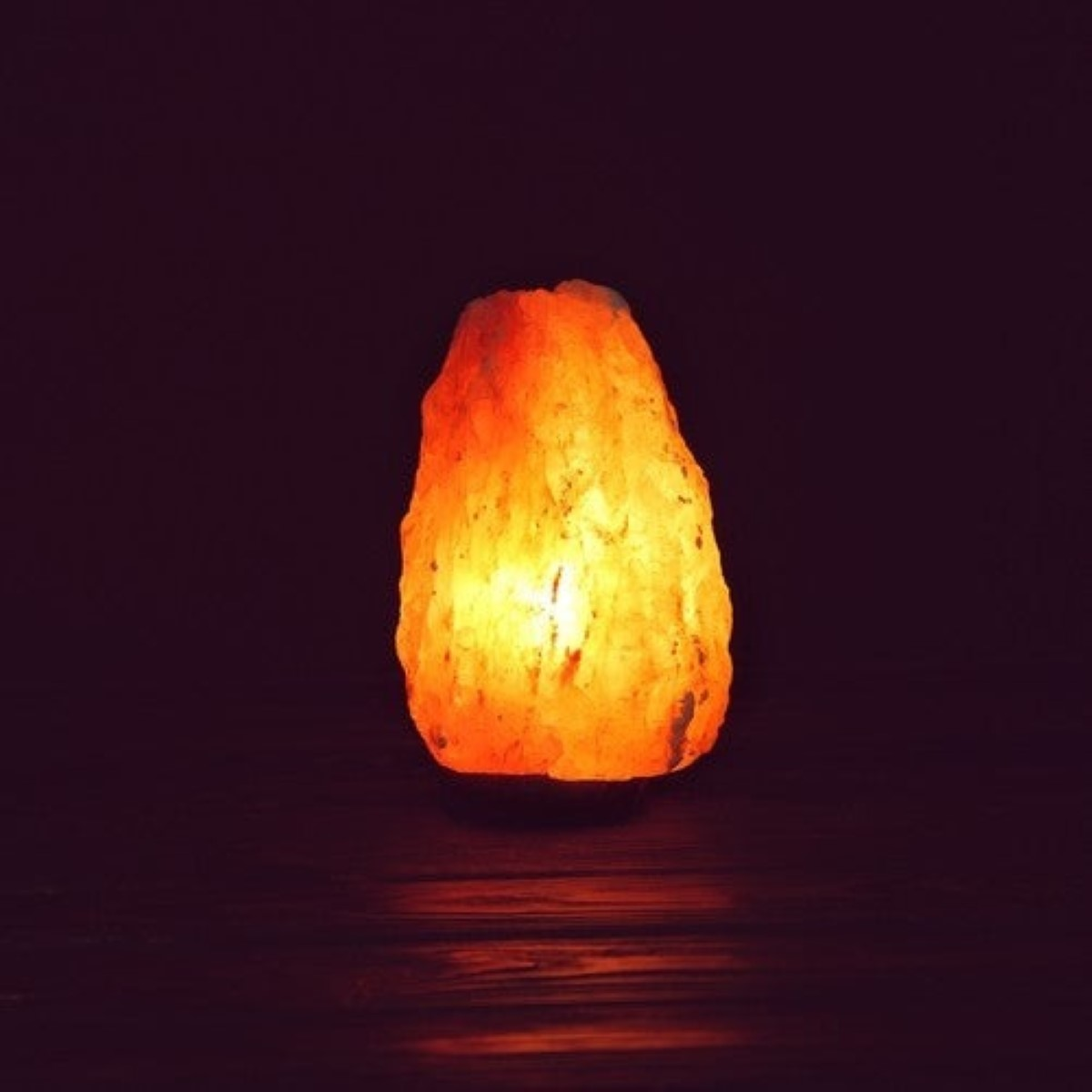Una lámpara de sal del Himalaya iluminada descansa sobre una superficie de madera oscura.