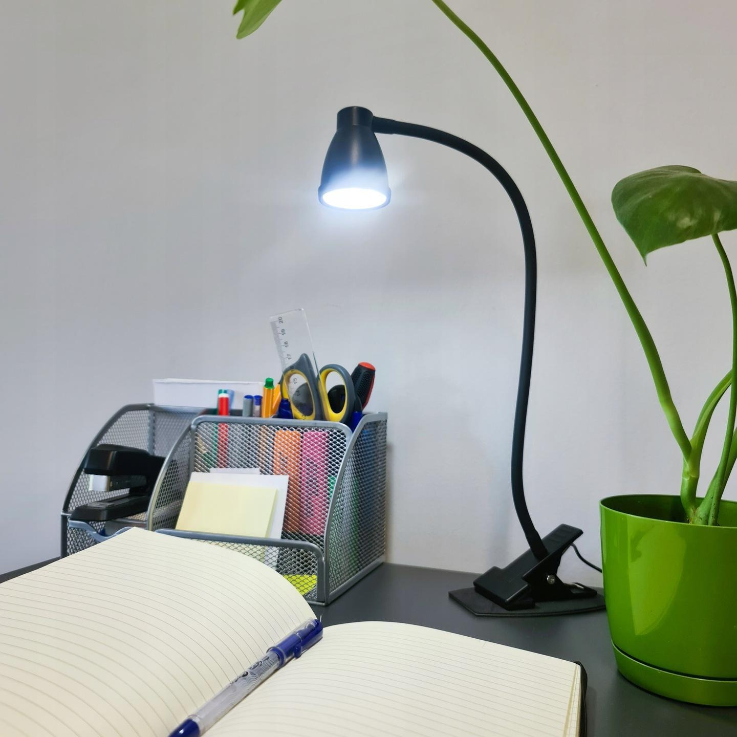 Escritorio con lámpara, cuaderno, bolígrafos, tijeras y planta.