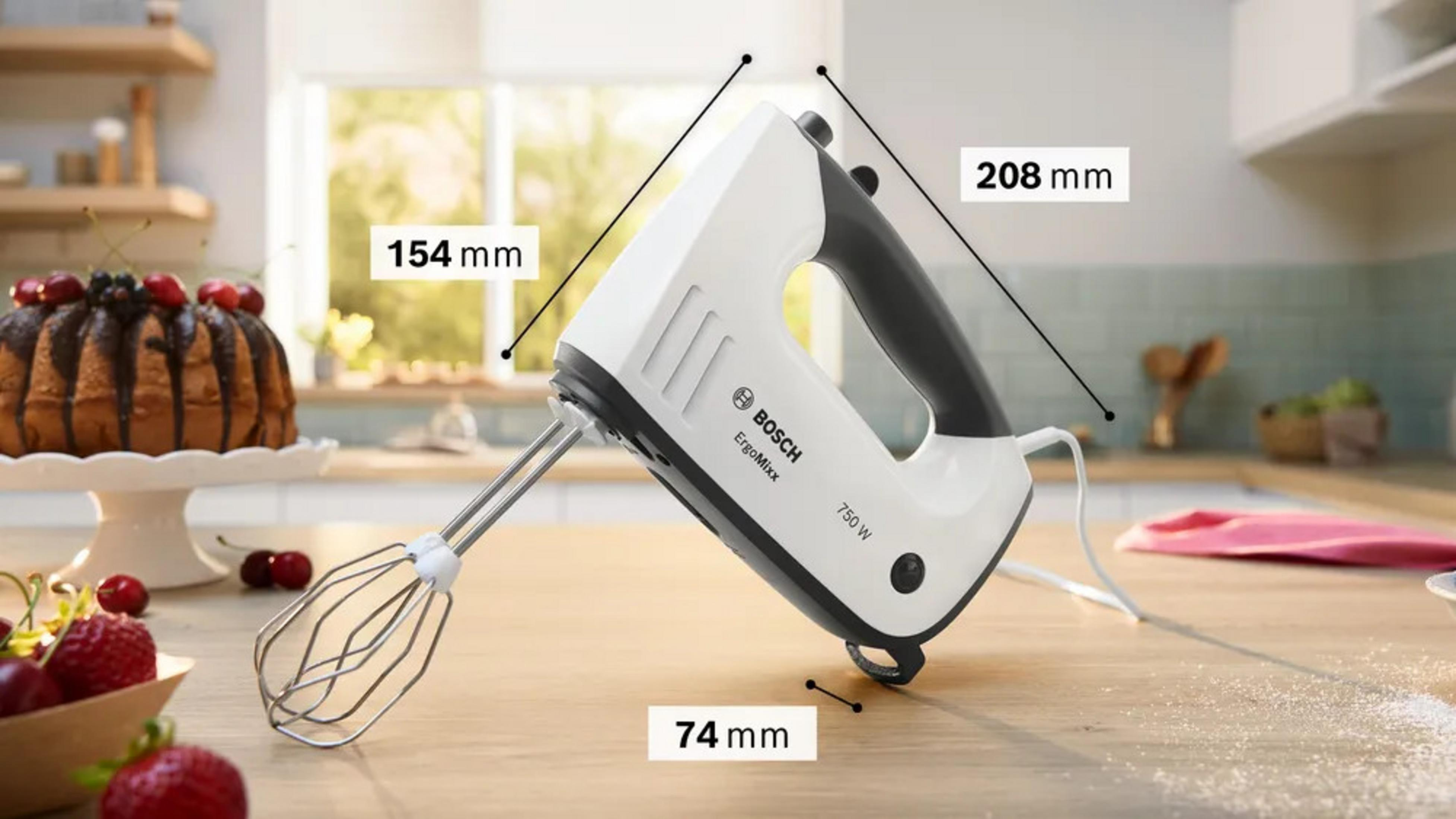 Ein weißer Bosch Handmixer mit schwarzem Griff steht auf einem Holztisch neben einem Kuchen.