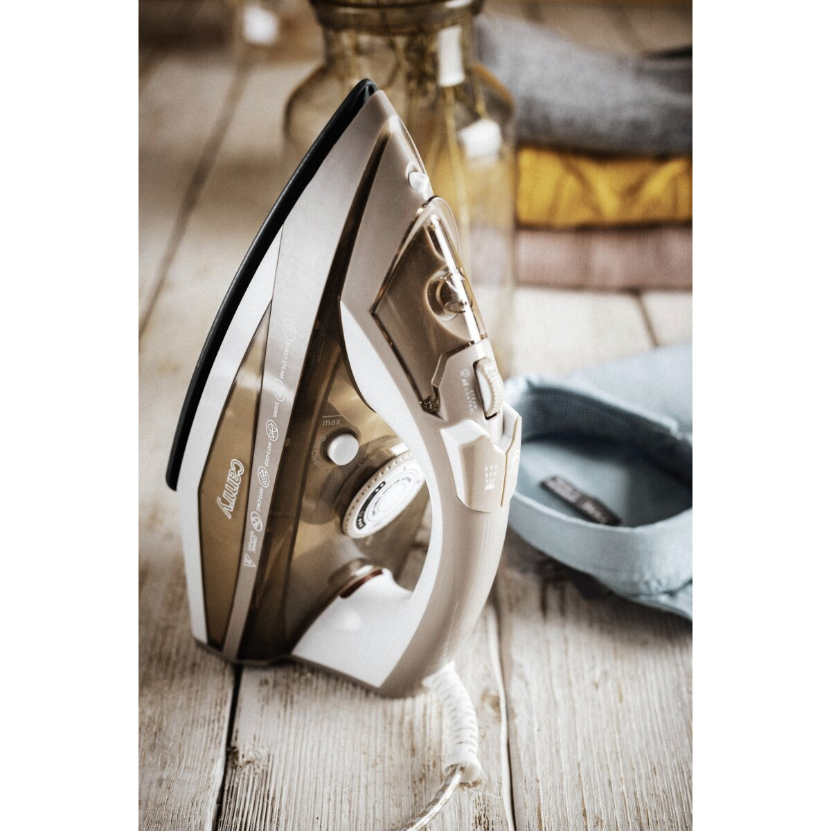Żelazko z kablem i tkaninami w tle na drewnie.