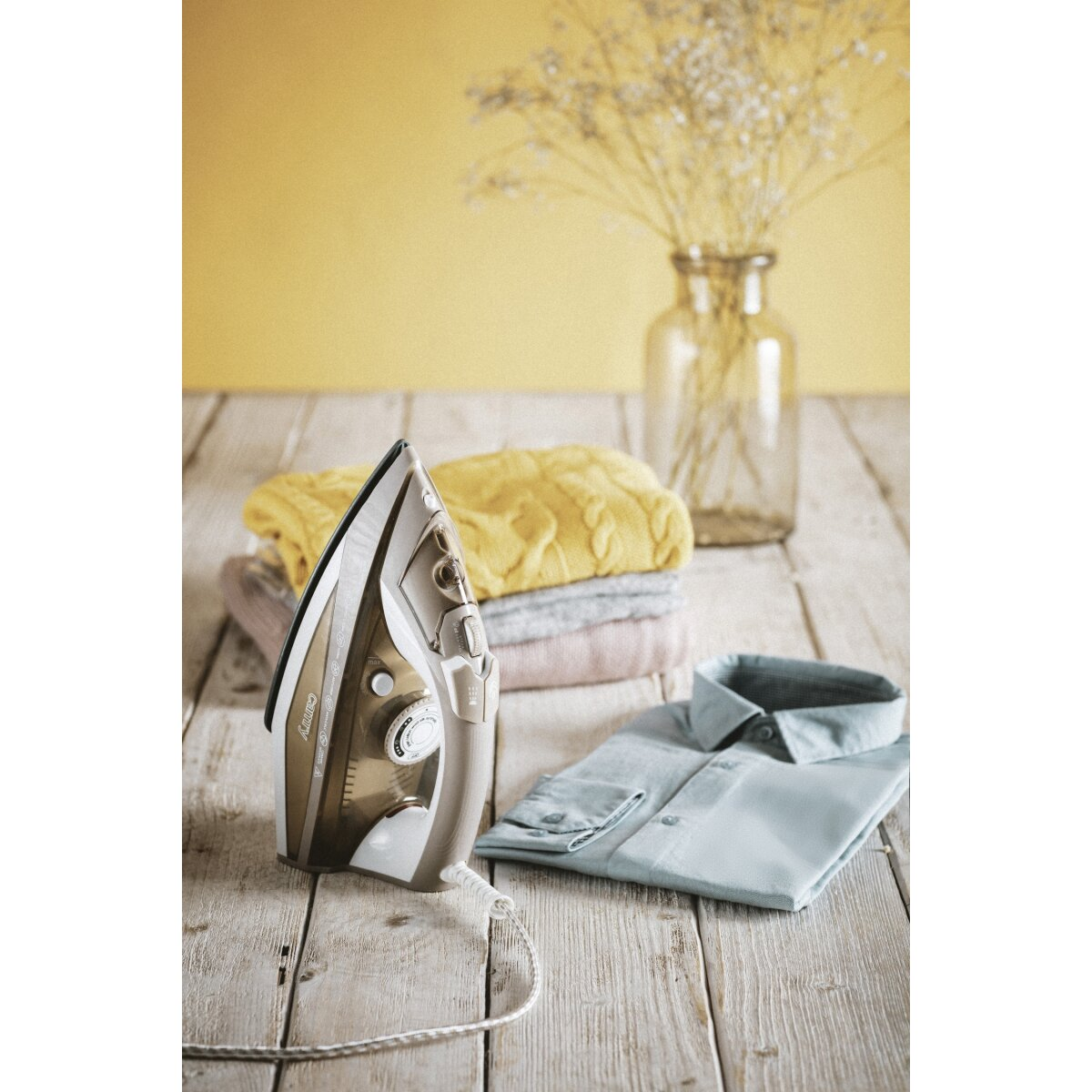 Żelazko obok stosu ubrań i koszuli na drewnianym stole.