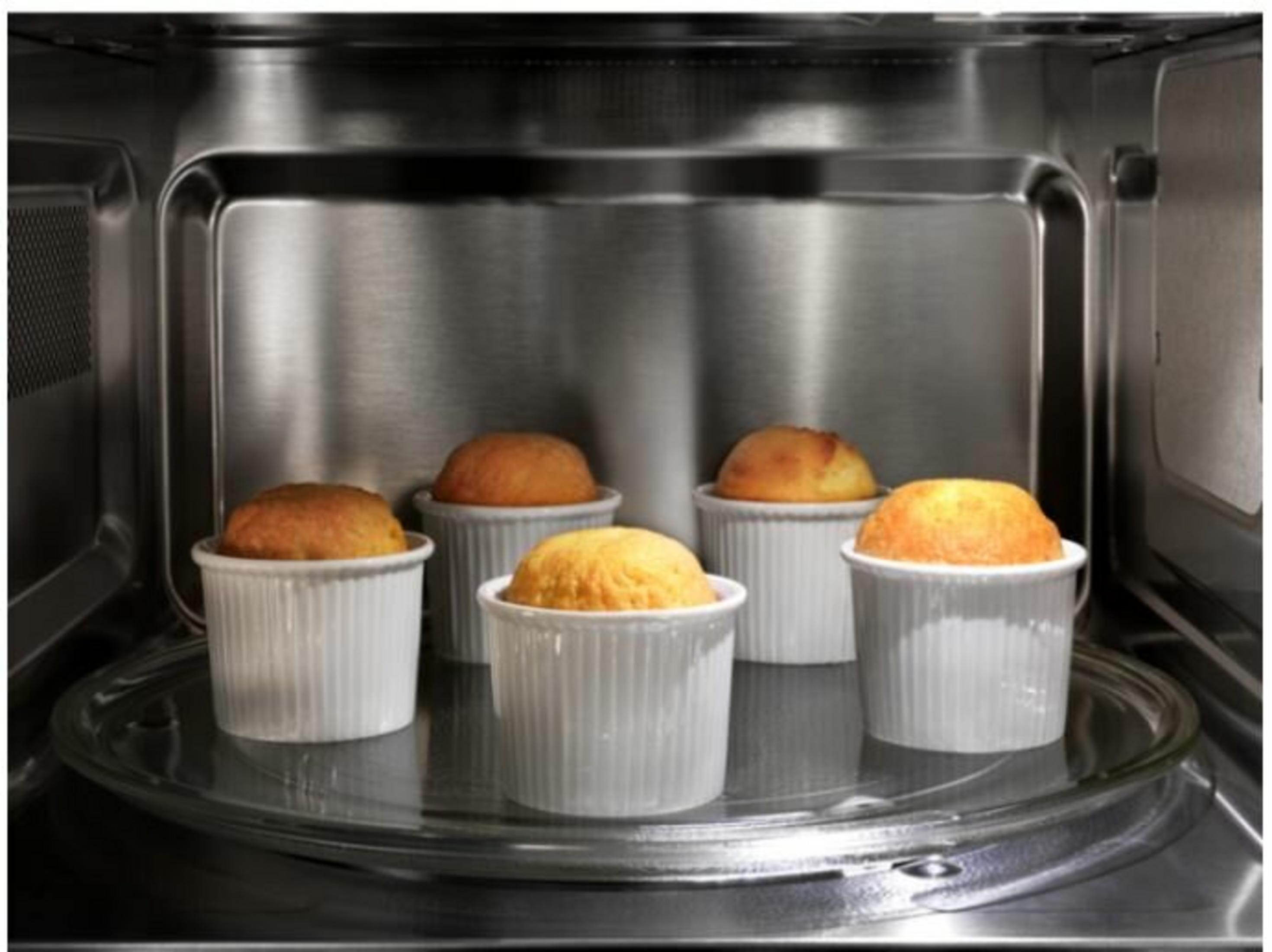 Pięć złocistobrązowych muffinek w białych foremkach w kuchence mikrofalowej.