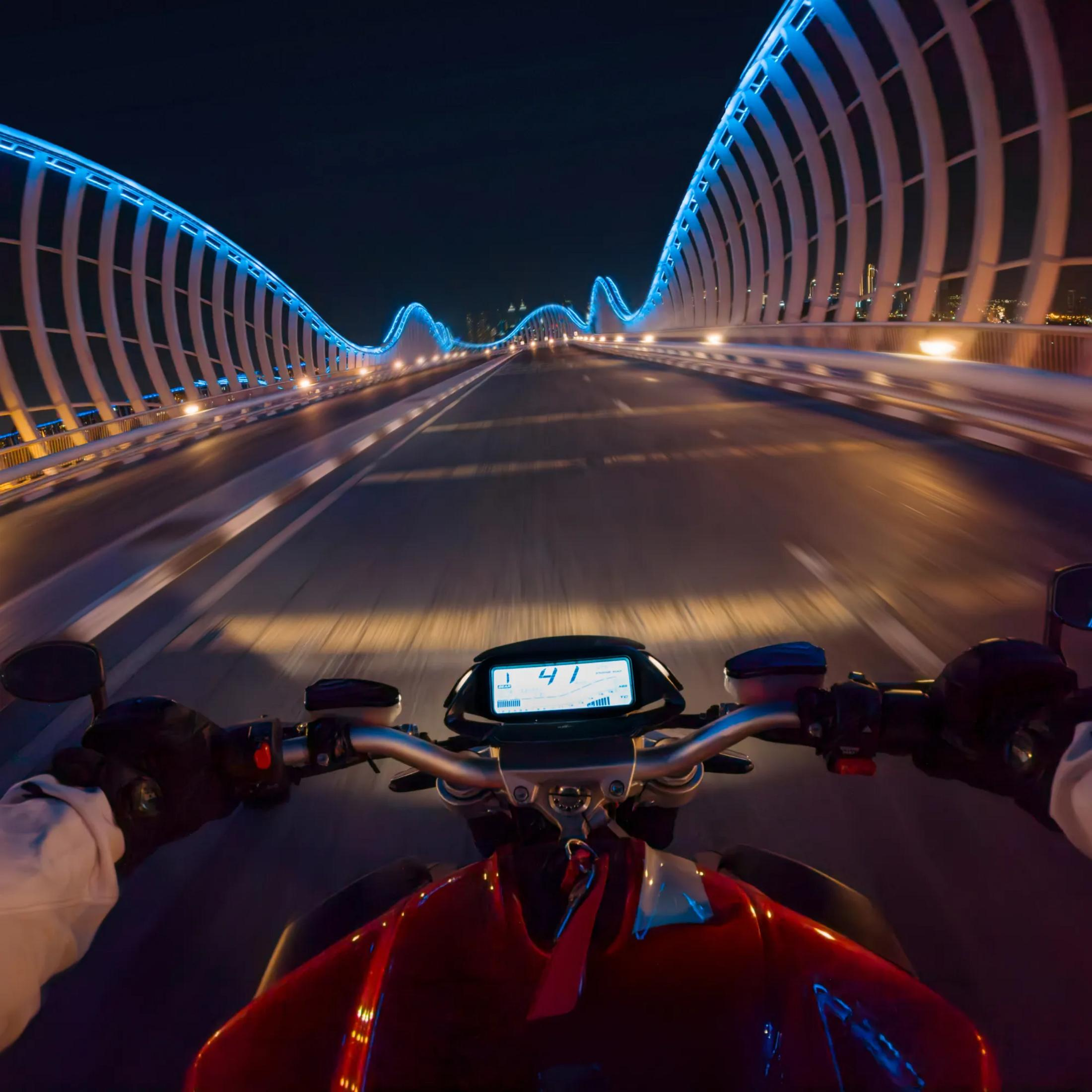 Motosikletçi gece aydınlatmalı köprüden geçiyor, göstergede 41 km/s.