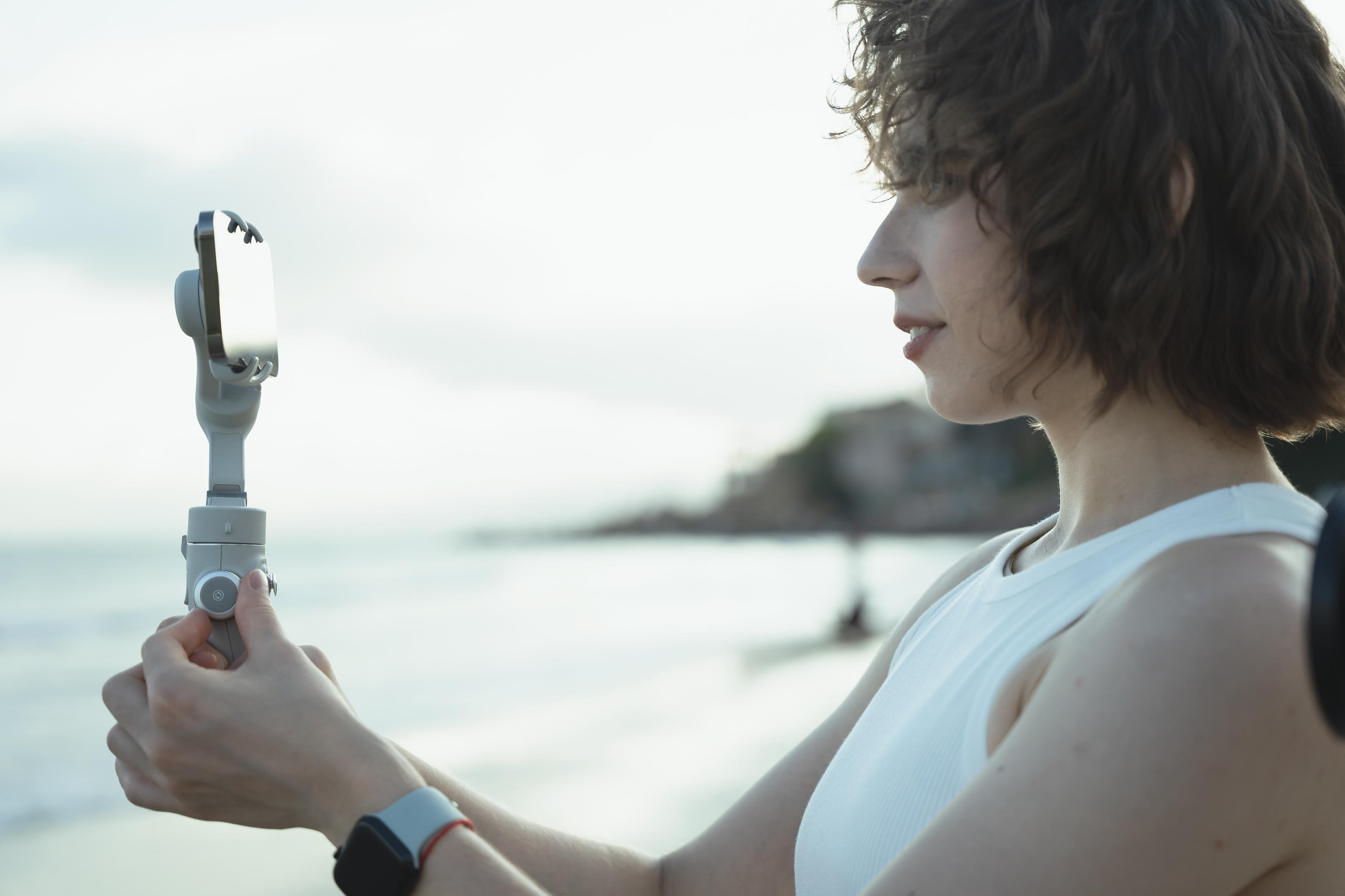 Une femme tient un stabilisateur de téléphone sur la plage au coucher du soleil.