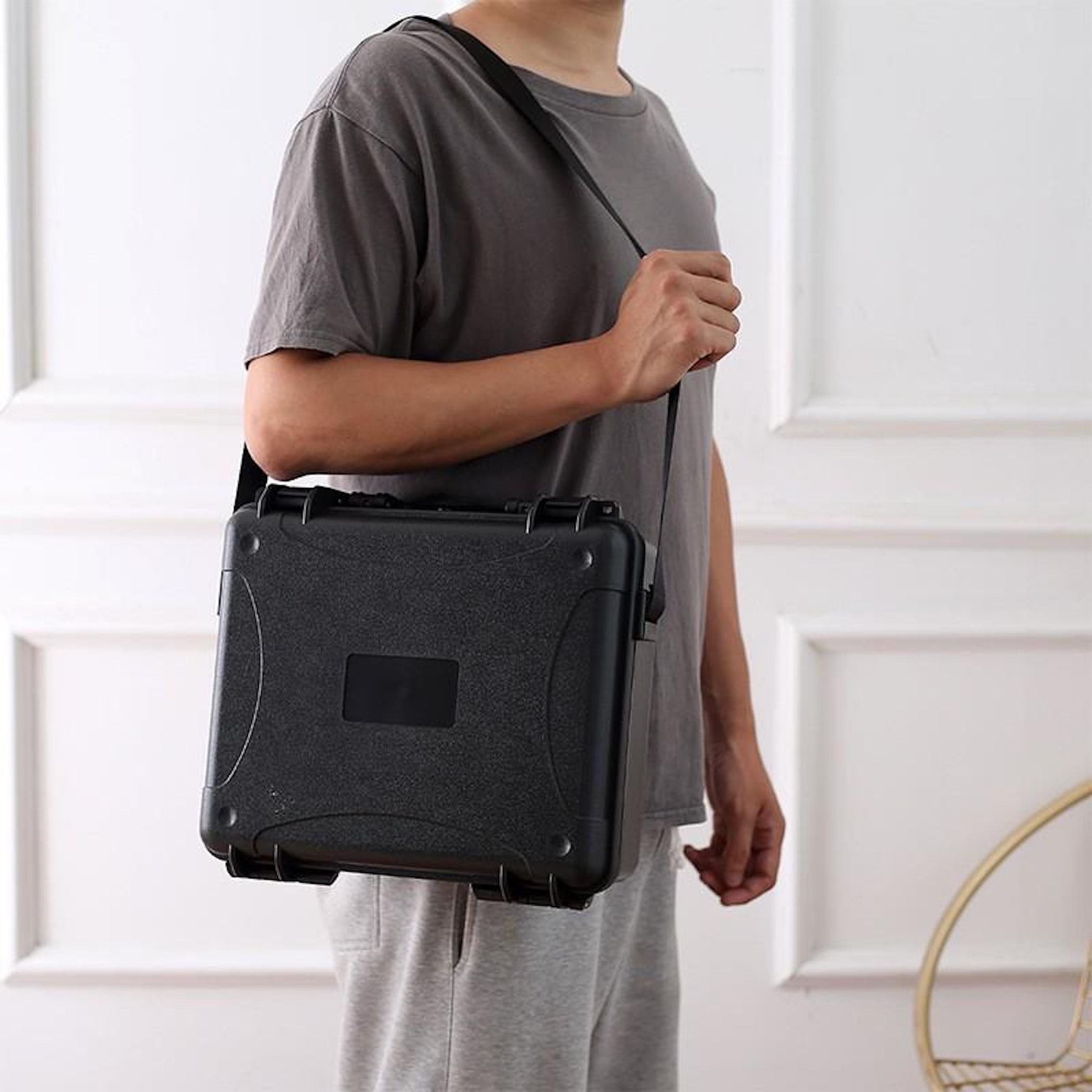 Person trägt schwarze Tasche über der Schulter, graues T-Shirt, weiße Wand.