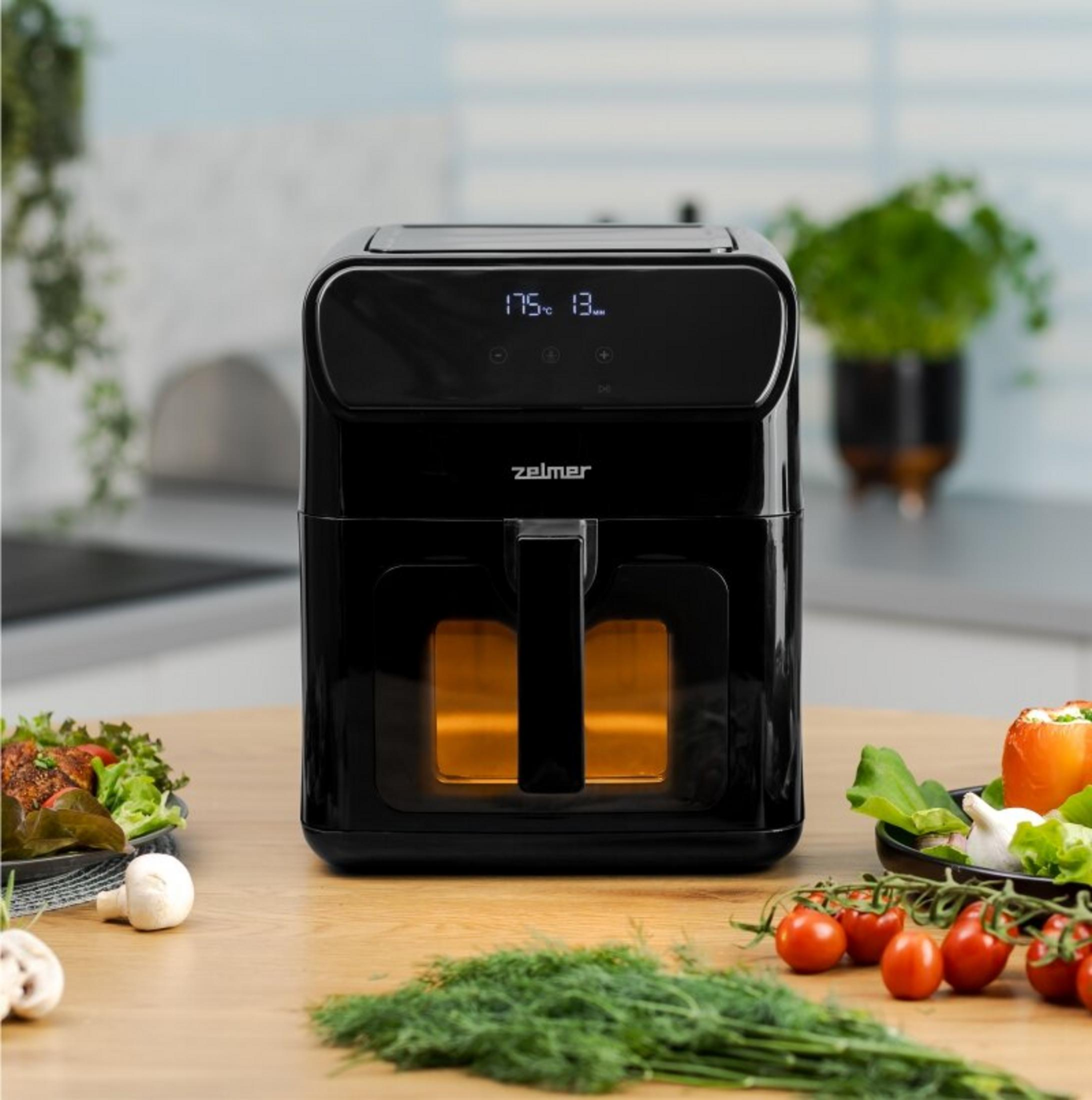 Friggitrice ad aria Zelmer nera con interno luminoso, accanto a verdure.