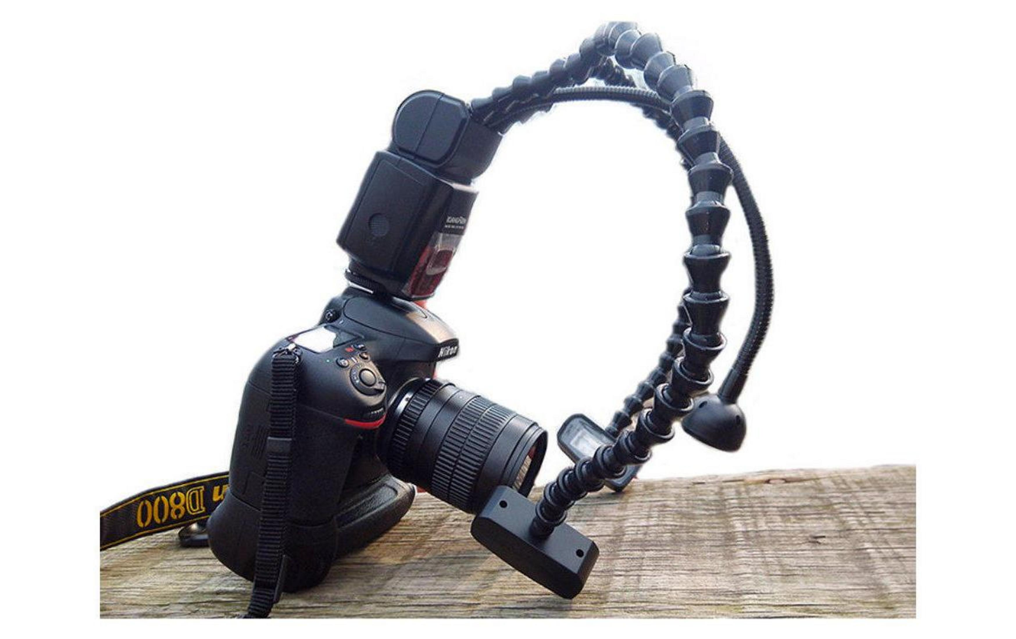 Una fotocamera Nikon D800 nera con flash su braccio flessibile su legno.