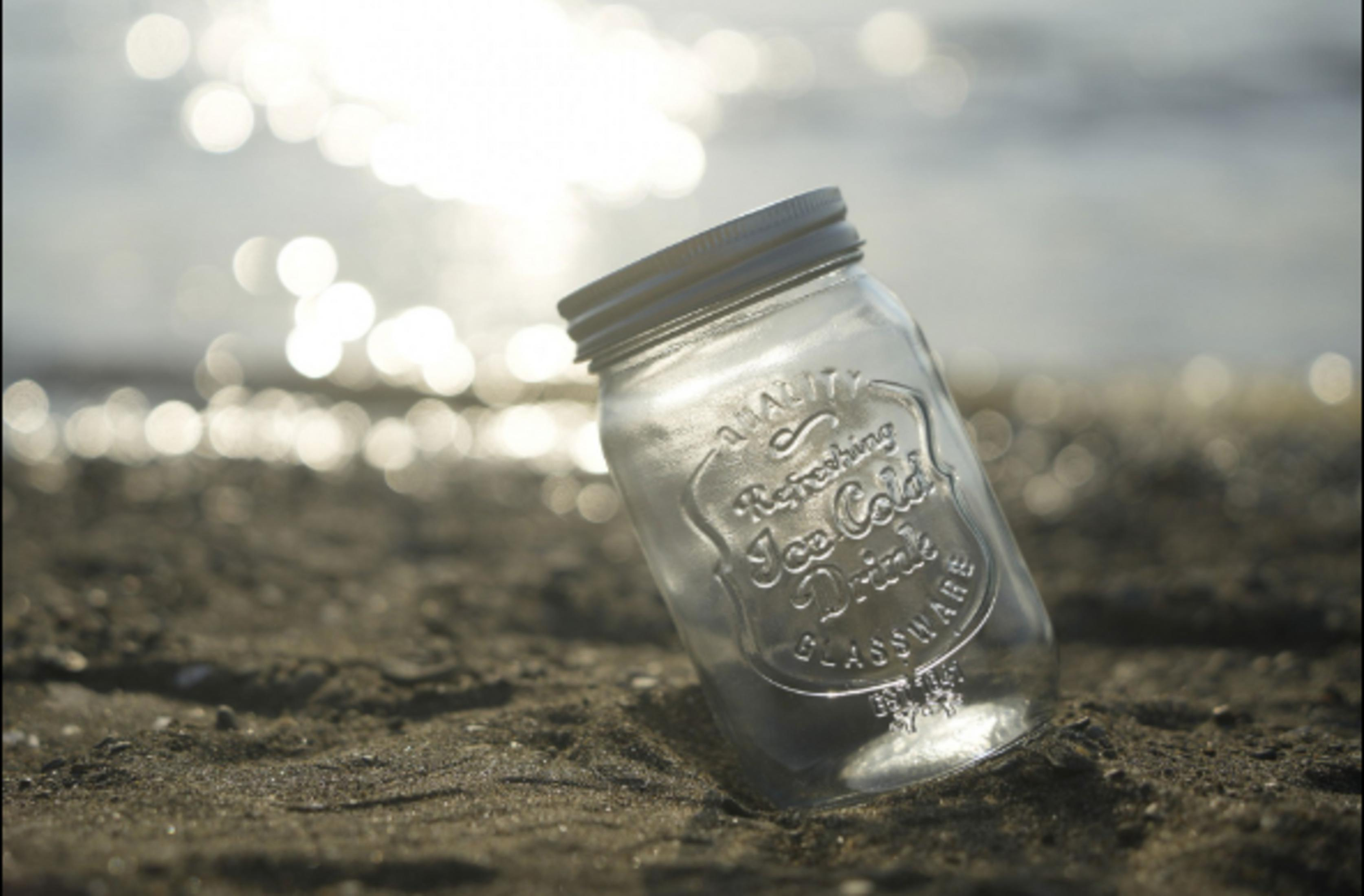 Ein leeres Glas liegt im Sand am Strand mit der Sonne im Wasser.