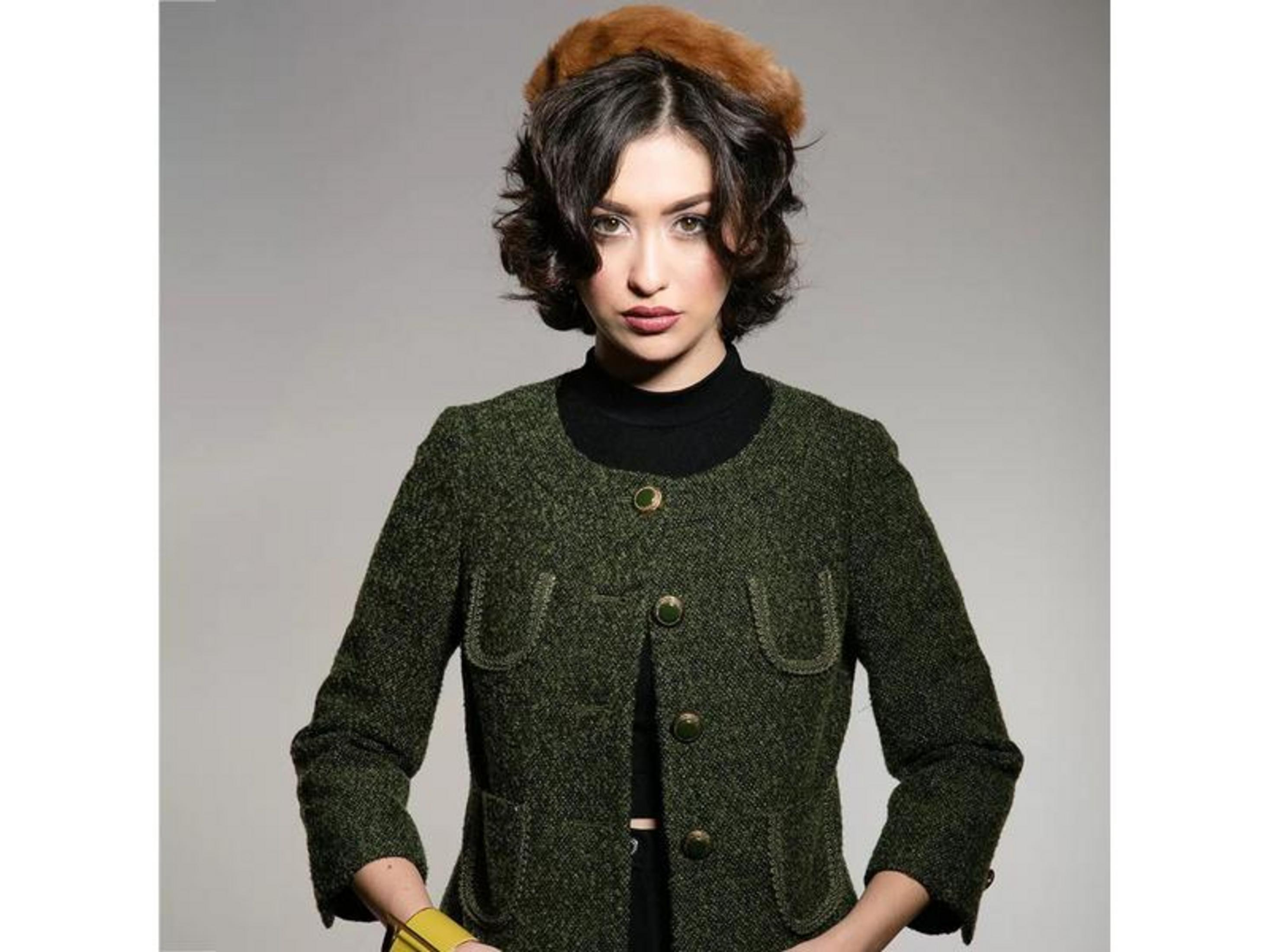 Une femme aux cheveux bruns courts porte un blazer en tweed vert et un chapeau de fourrure.
