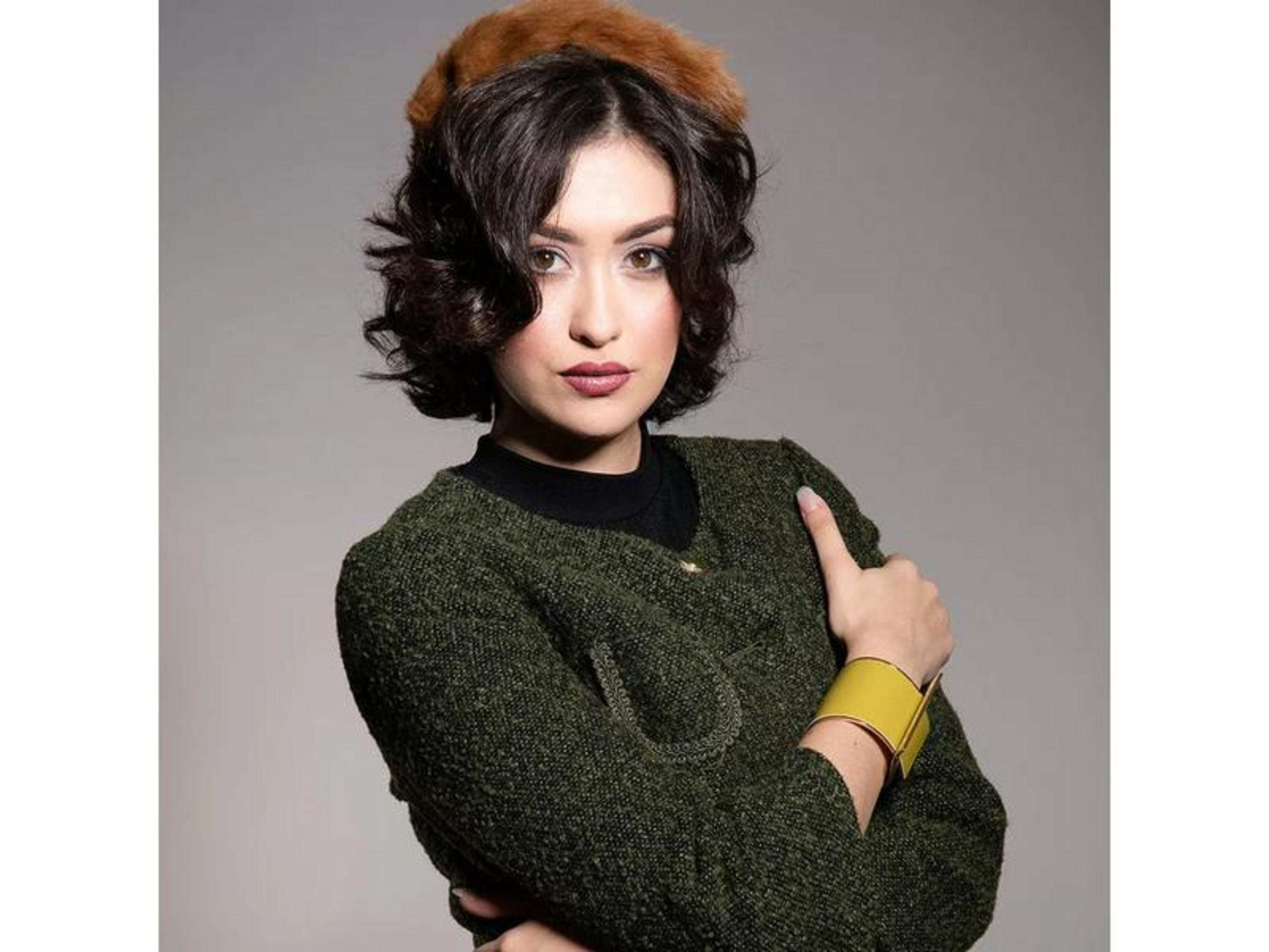 Femme aux cheveux bruns, bonnet en fourrure, veste verte et bracelet jaune.
