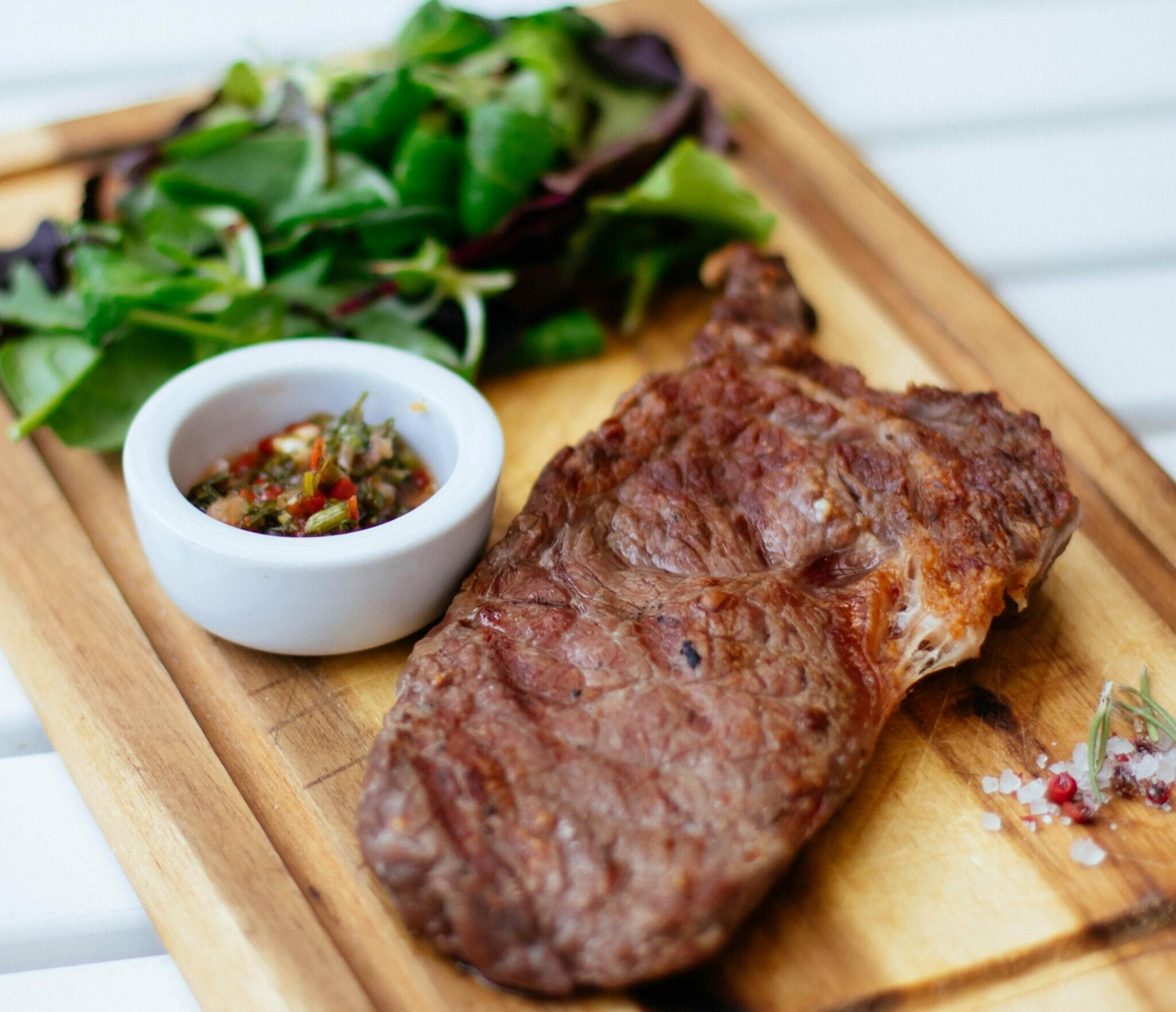 Grillowany stek z sałatką i sosem w miseczce, na desce drewnianej z solą.