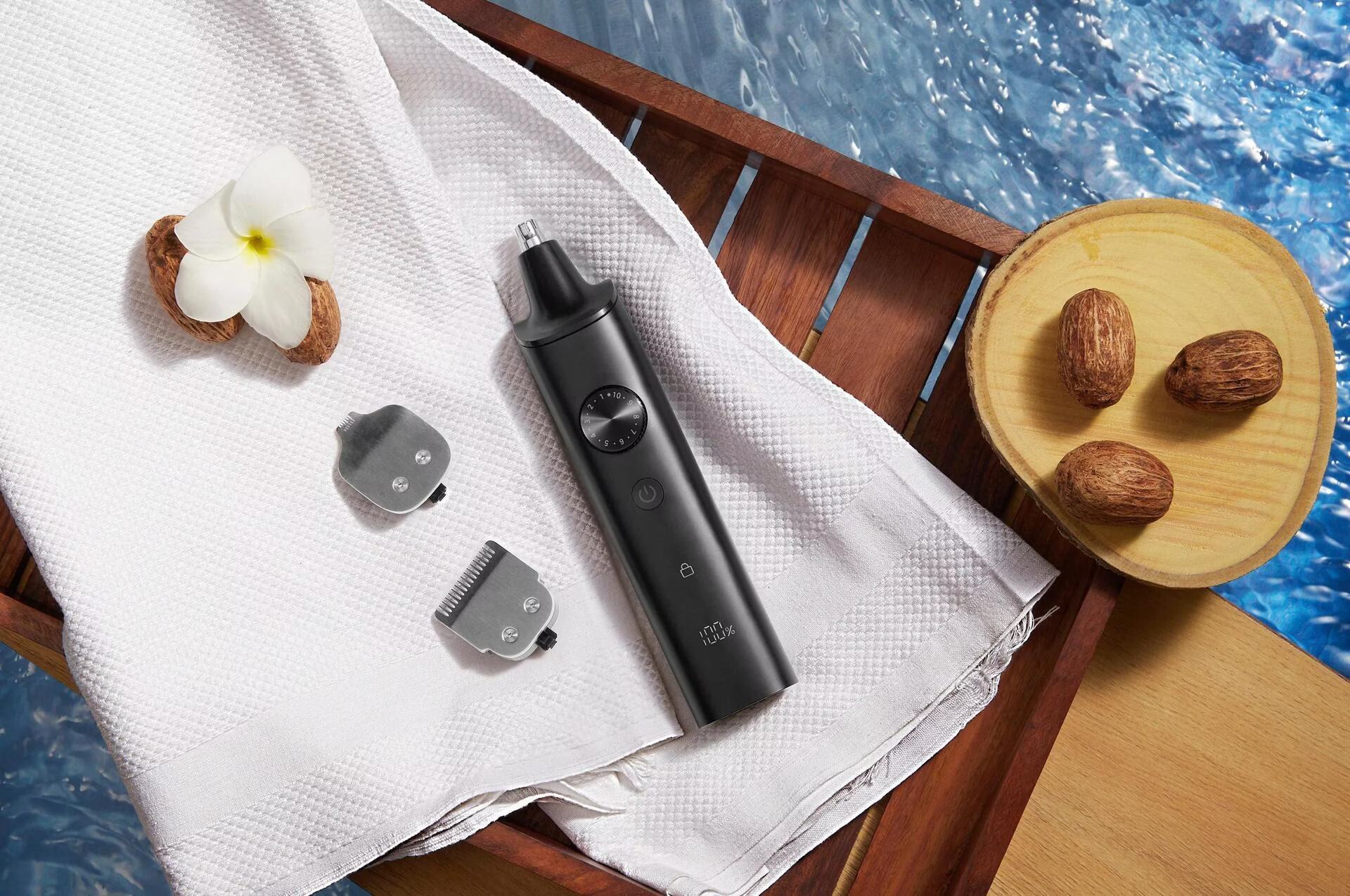 Ein schwarzer Trimmer mit Aufsätzen auf weißem Handtuch, daneben eine Blume und Nüsse.