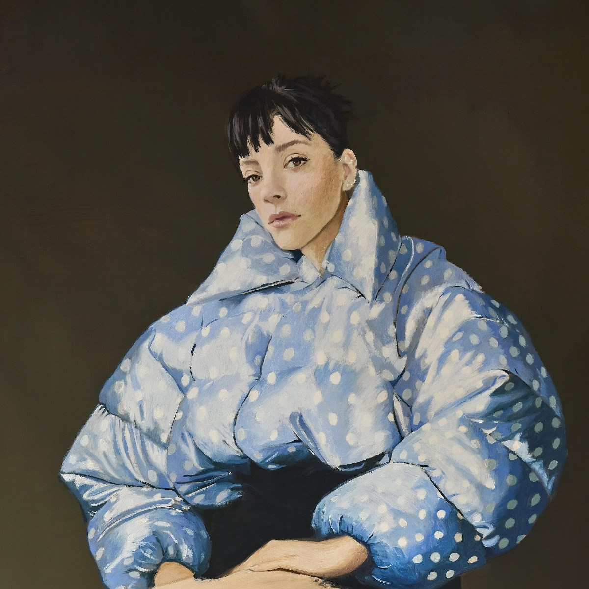Een vrouw met kort zwart haar draagt een blauwe pufferjas met stippen. Donkere achtergrond.