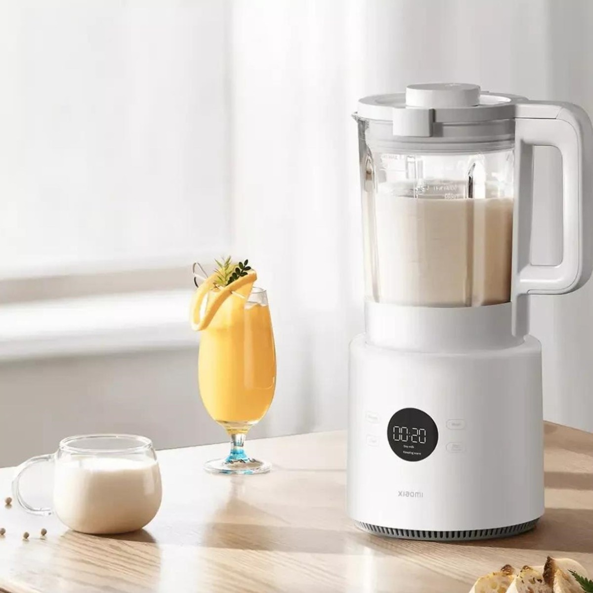 Un frullatore bianco con un bicchiere di succo e una tazza di latte su un tavolo di legno.