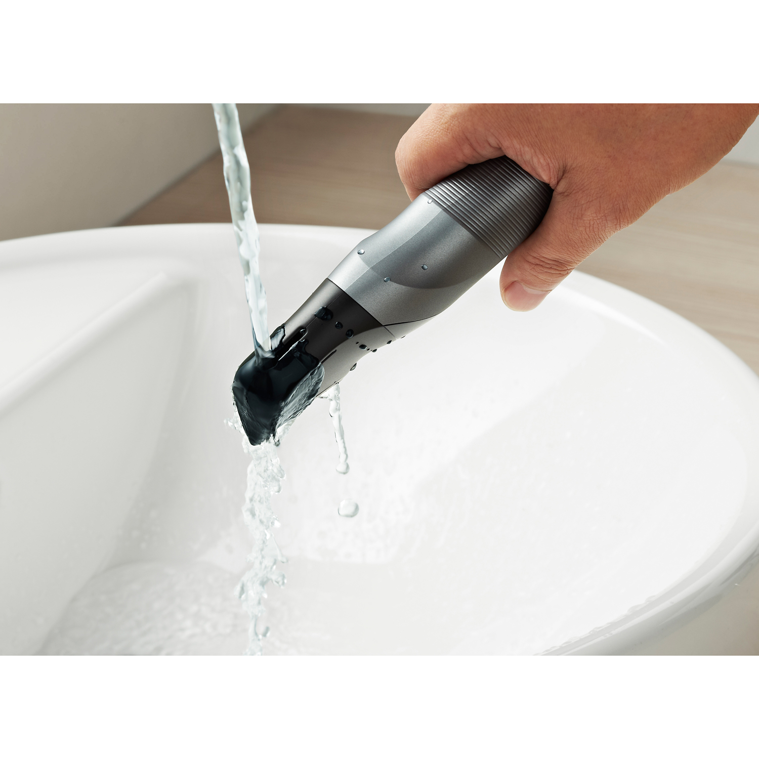 Una mano sciacqua un rifinitore sotto acqua corrente in un lavandino bianco.