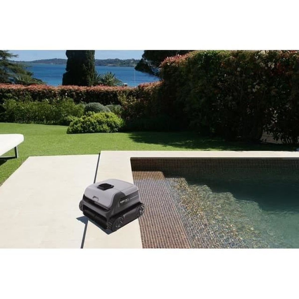 Ein grauer Roboter-Poolreiniger sitzt am Rand eines gefliesten Pools, mit einem grünen Rasen und Wasser im Hintergrund.