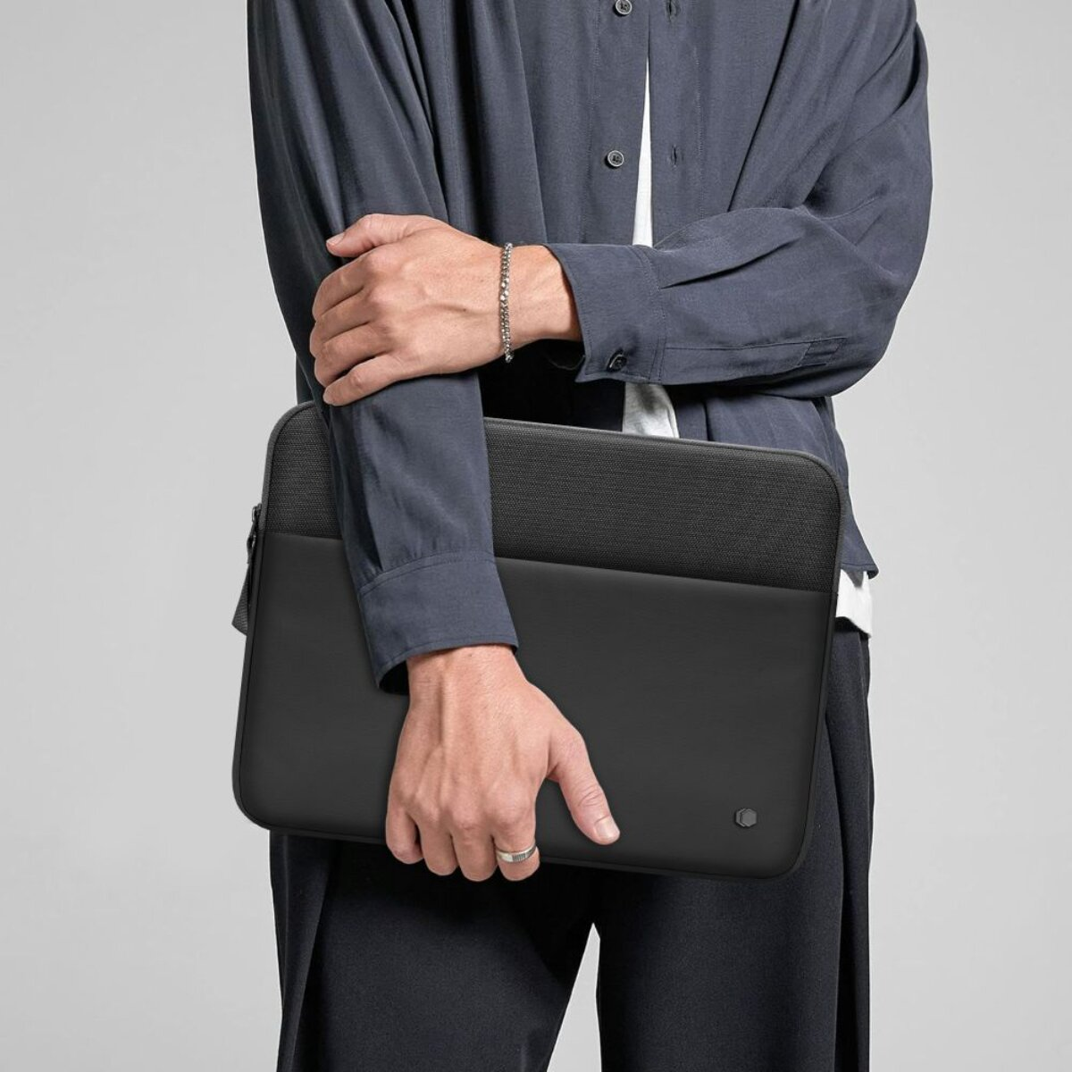 Mann hält eine schwarze Laptoptasche, trägt ein blaues Hemd und eine weiße Weste.