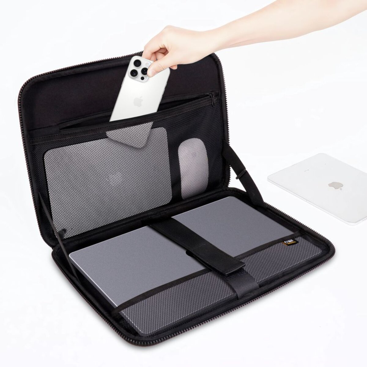 Eine Hand legt ein silbernes iPhone in einen schwarzen Tech-Organizer mit Laptop, Tablet und Maus.