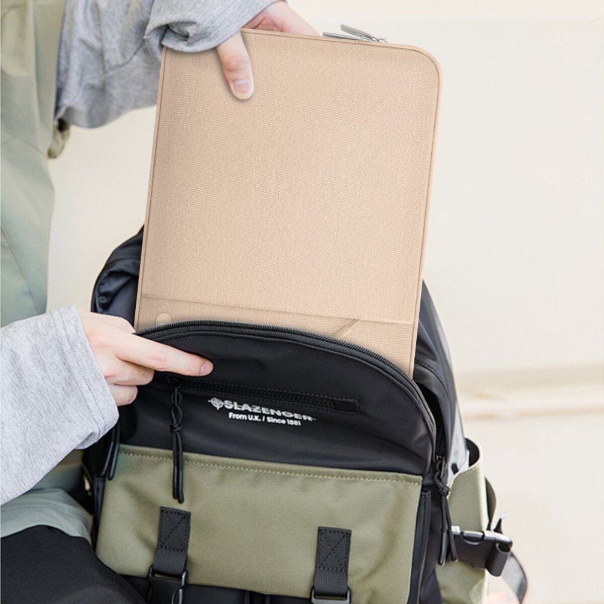 Eine Person steckt eine beige Laptoptasche in einen Rucksack.