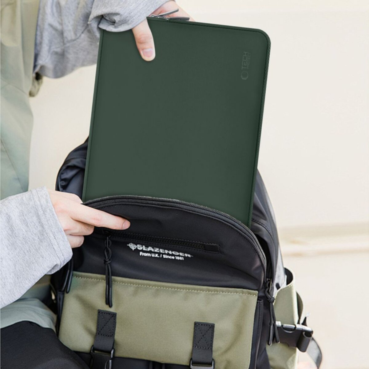 Eine Person legt eine grüne Laptoptasche in einen Rucksack.
