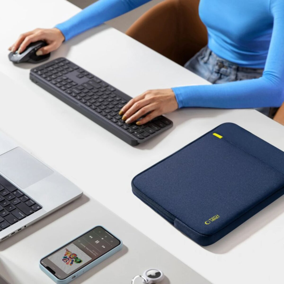 Eine Person tippt auf einer Tastatur, daneben ein Laptop, Handy, Maus und eine Tasche.