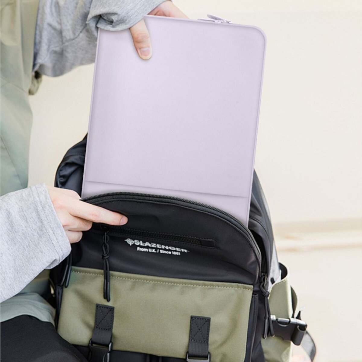 Eine Person steckt eine hellviolette Hülle in einen Rucksack mit grünen und schwarzen Teilen.