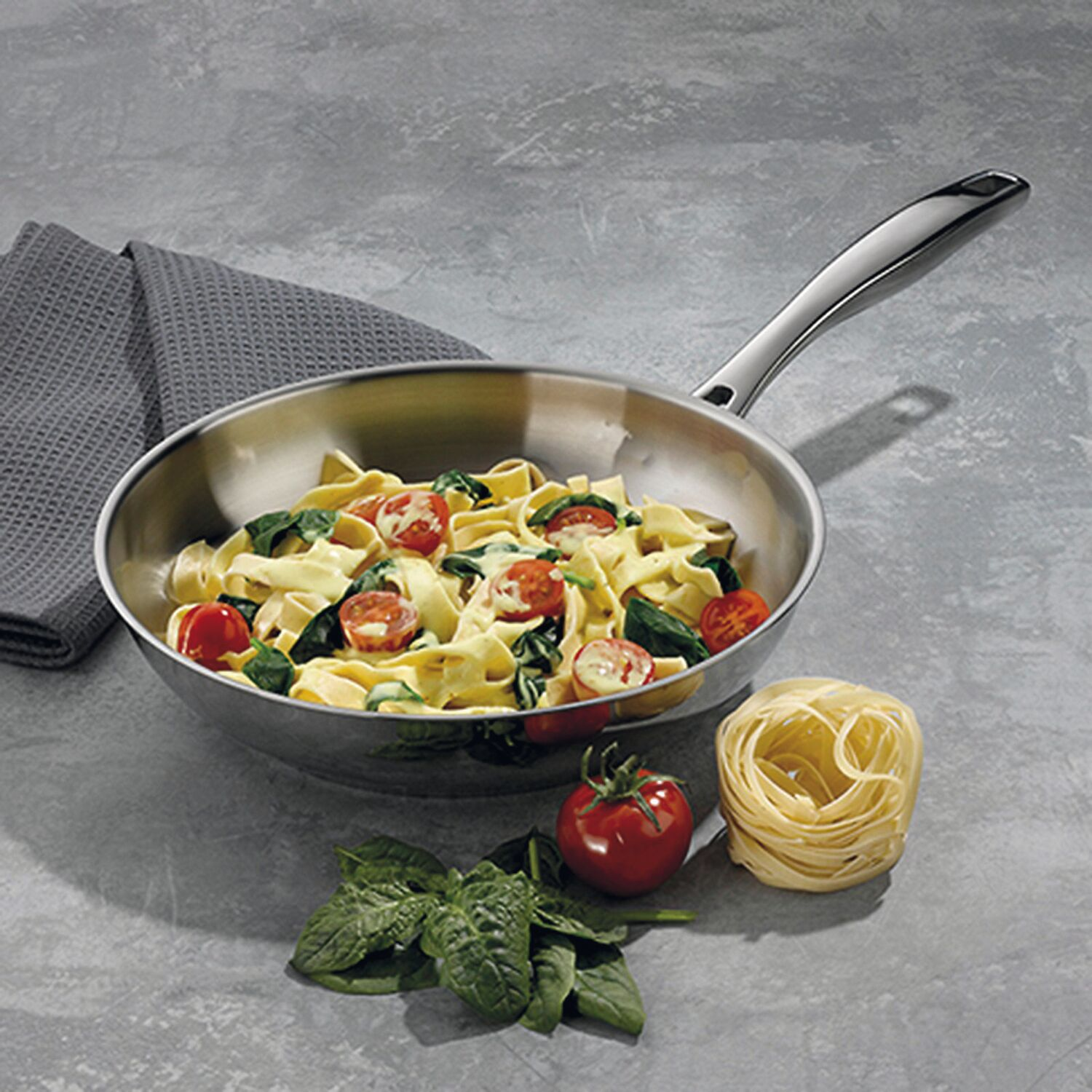 Pasta mit Spinat und Tomaten in einer Pfanne, daneben rohe Zutaten.