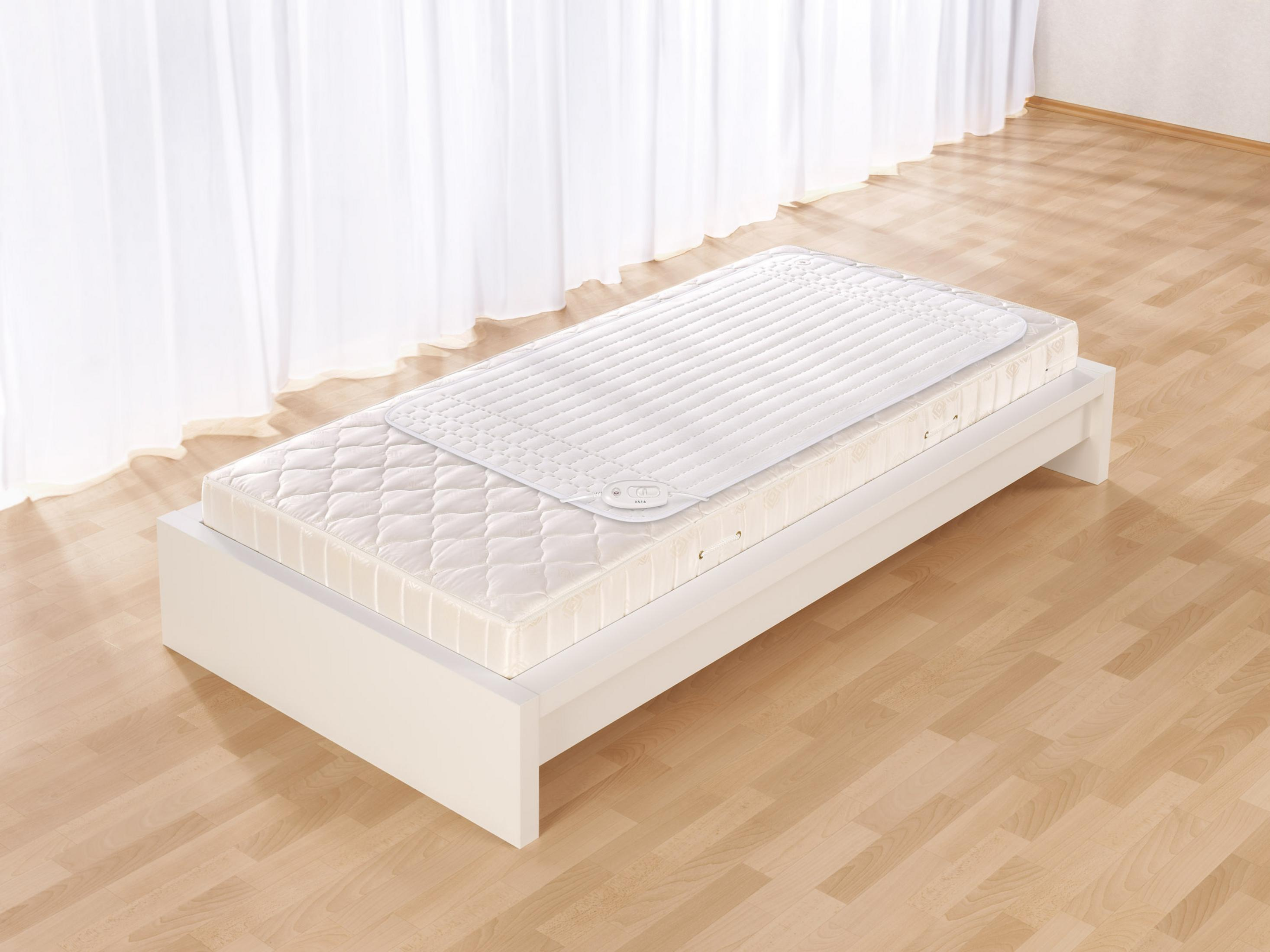 Un letto bianco con materasso e coperta riscaldata davanti a una tenda.