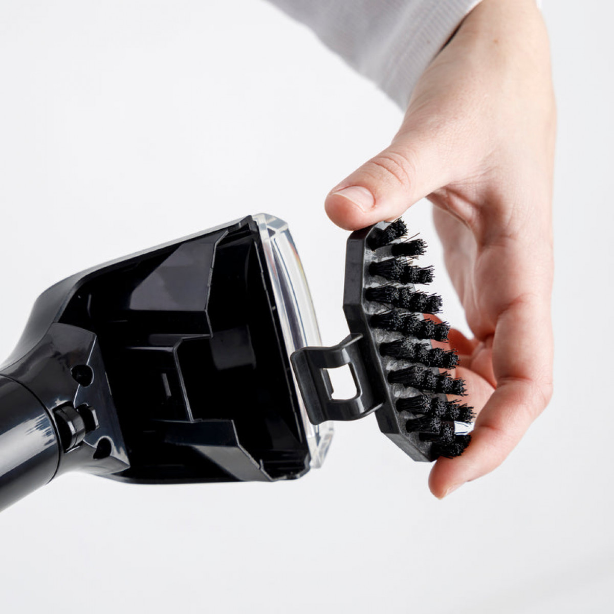 Ręka trzyma czarną szczotkę, którą mocuje do czarnego urządzenia.