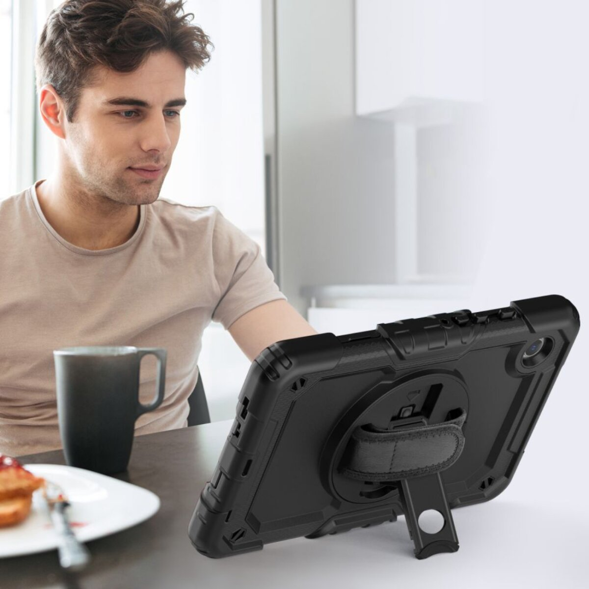 Mann sitzt am Tisch mit Tablet und Kaffee. Ein Toast mit Marmelade liegt auf einem Teller.