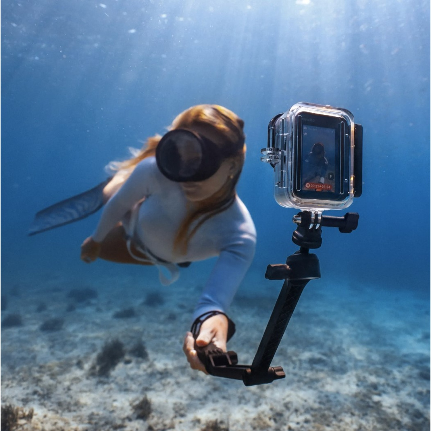Una donna si immerge sott'acqua con una telecamera che mostra il fondale.