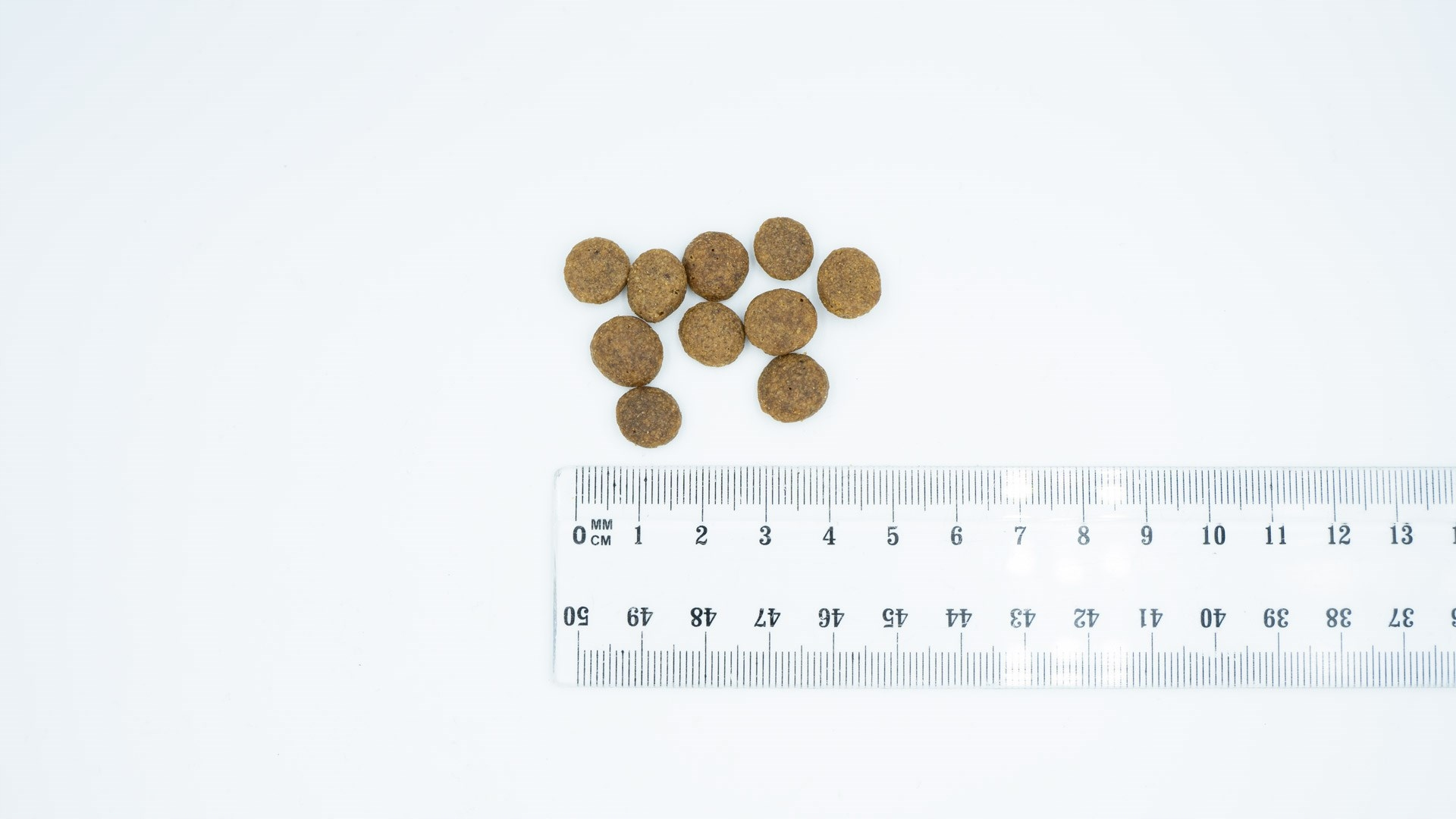 Dziesięć brązowych granulek obok linijki na białym tle.