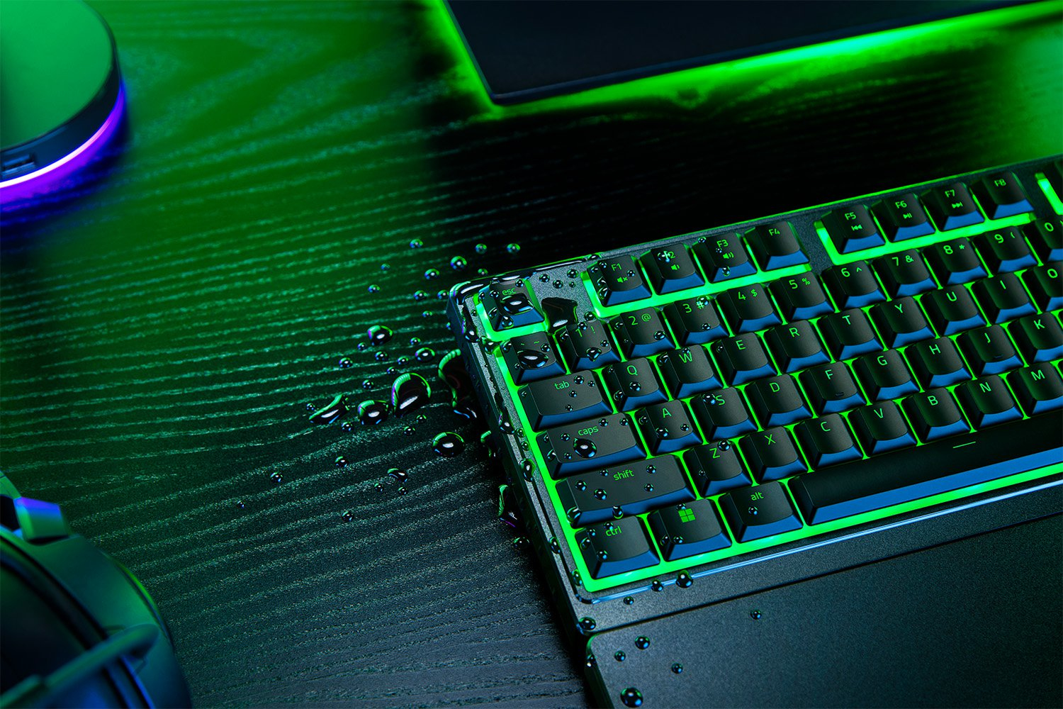 Gocce d'acqua su tastiera e scrivania retroilluminate di verde.