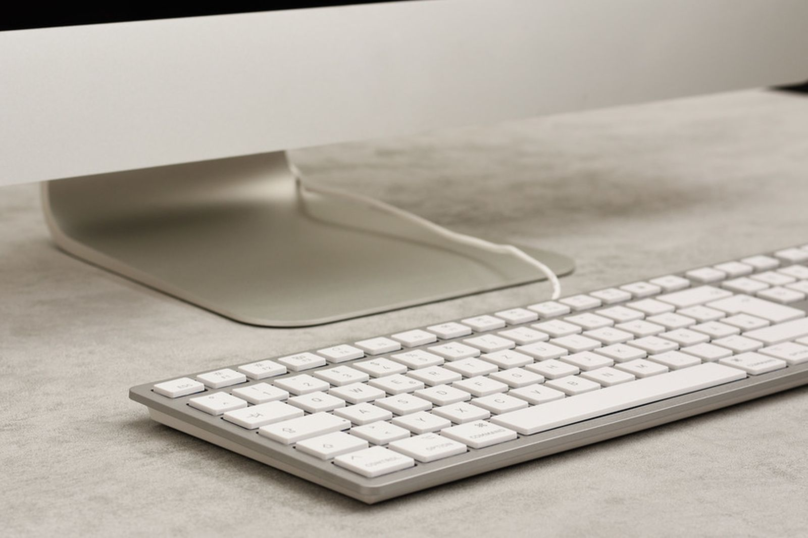Una tastiera argentata per computer poggia davanti al supporto di un monitor.