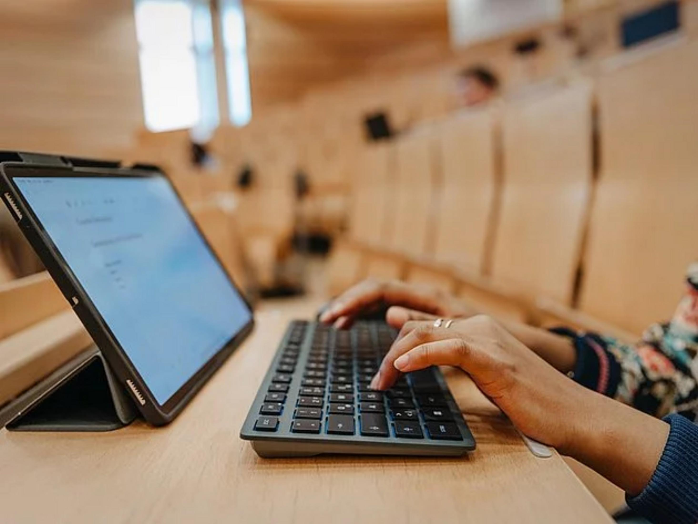 Eine Person tippt auf einer Tastatur, ein Tablet steht daneben.
