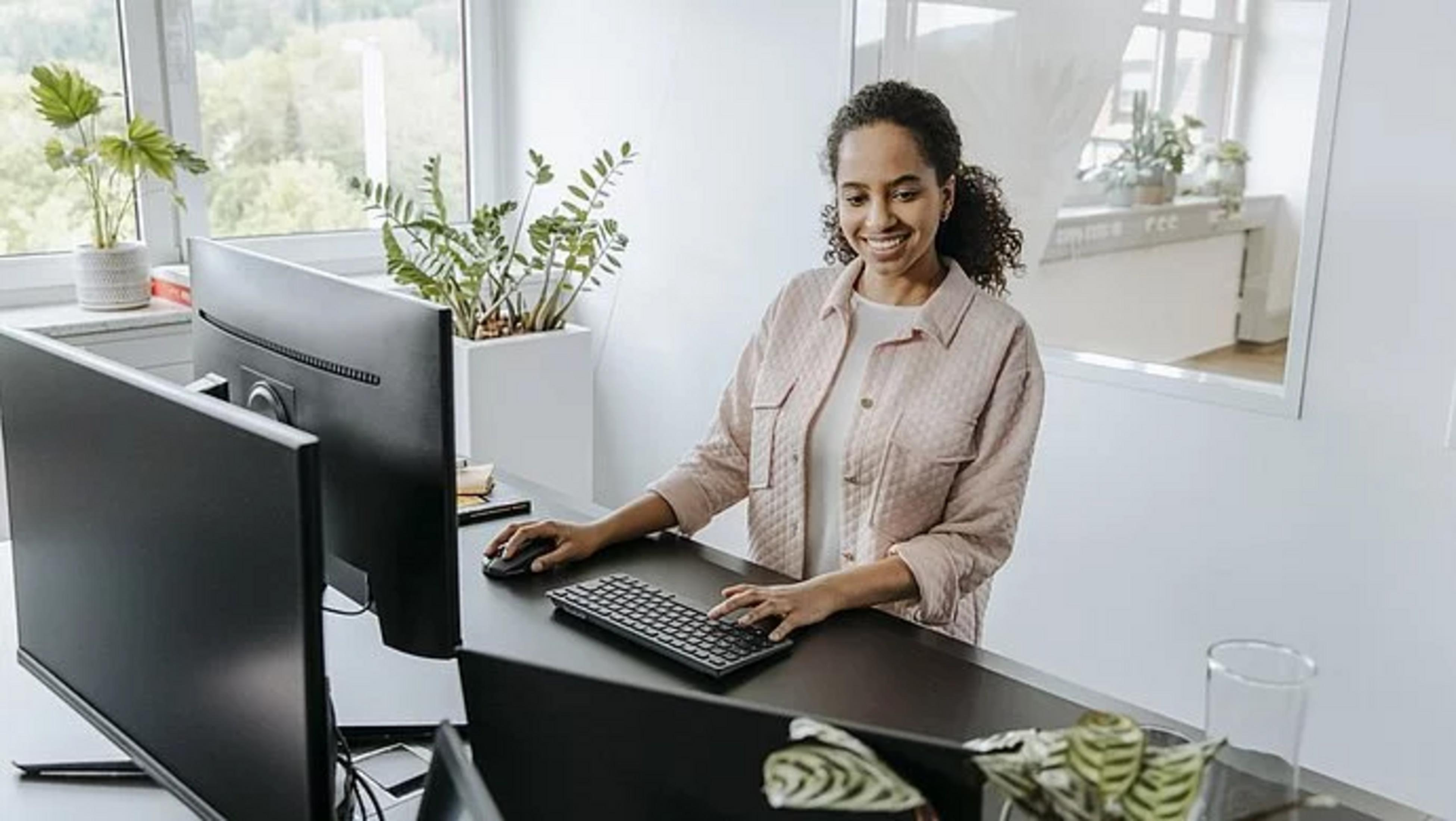 Frau arbeitet am Schreibtisch mit zwei Monitoren, Tastatur und Maus.