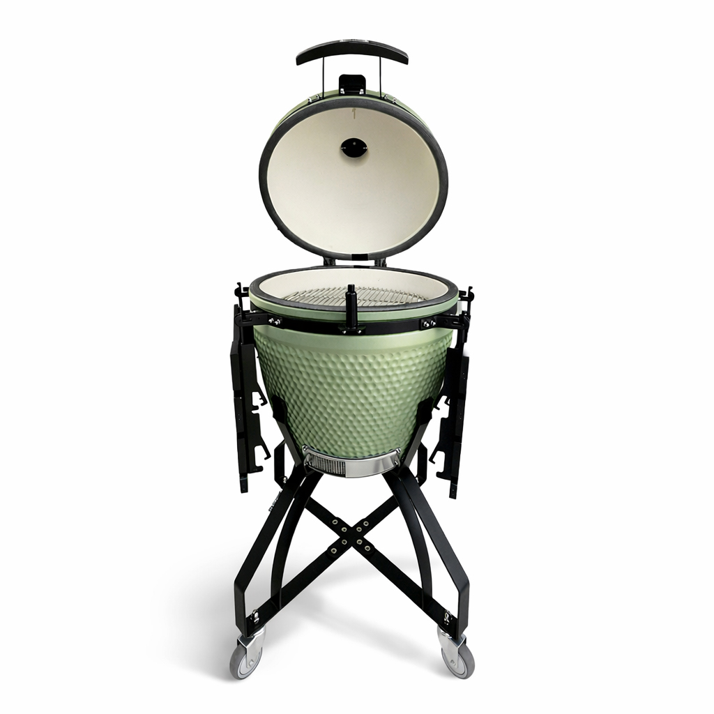 Een lichtgroene keramische kamado grill met open deksel, die een wit interieur en kookrooster onthult, staat op een zwart onderstel met wielen.