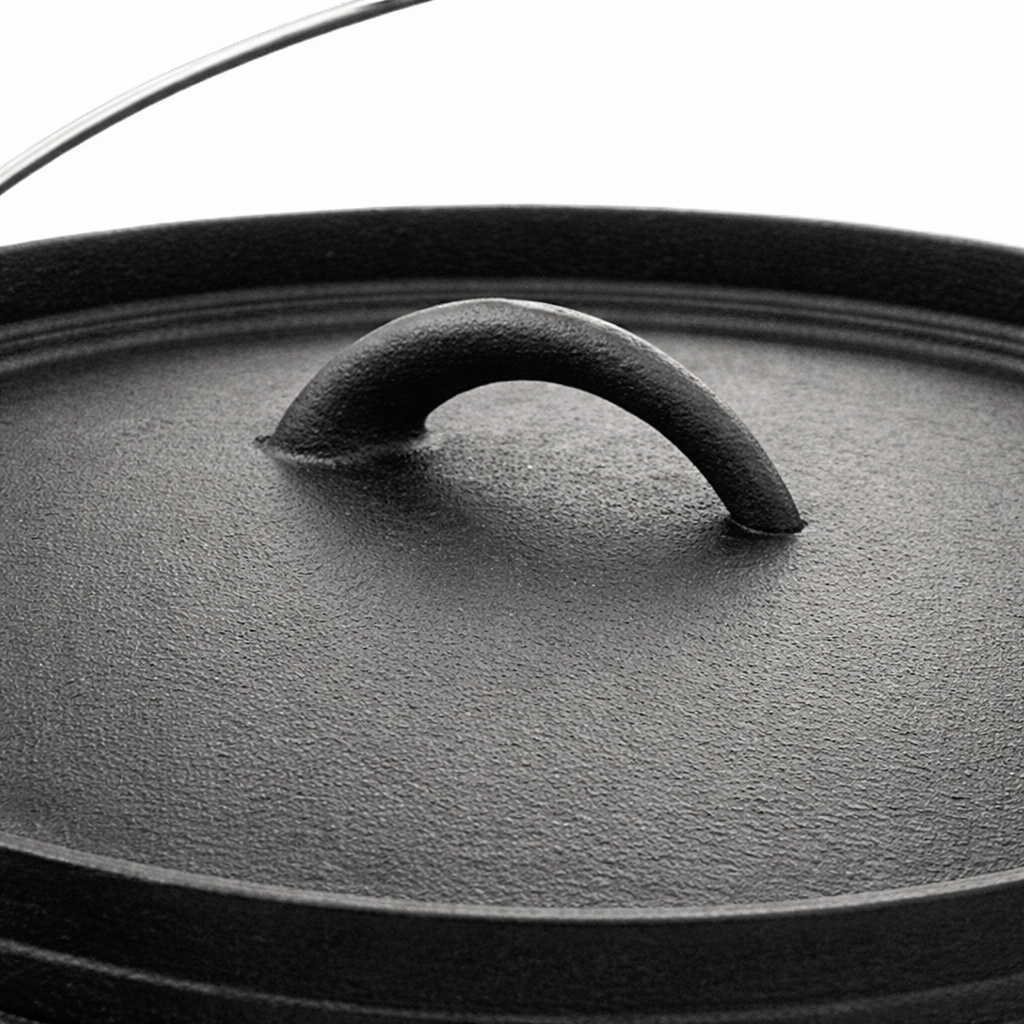 Close-up of a black cast iron Dutch oven lid with a curved handle and a wire bail handle in the background.