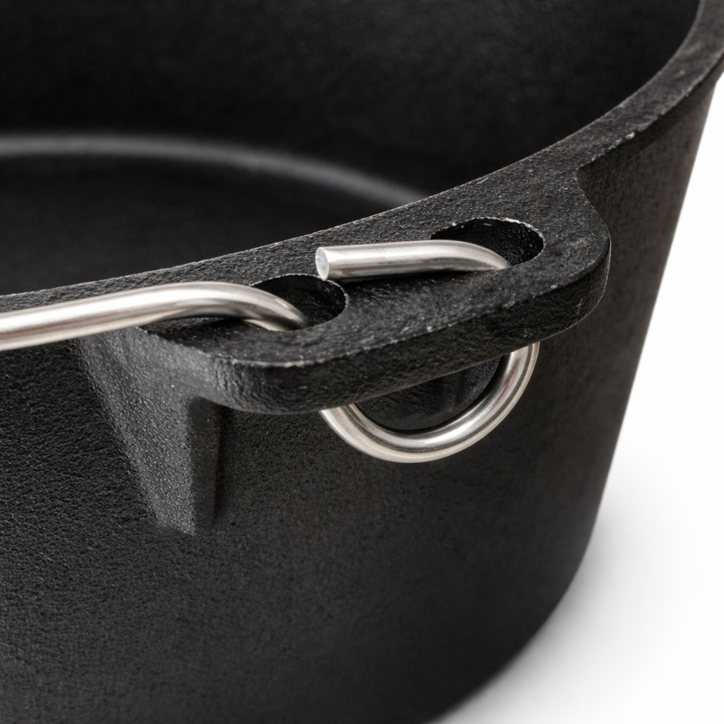 Close-up of a black cast iron pot's handle attachment. A silver metal wire loop connects to the pot's side.