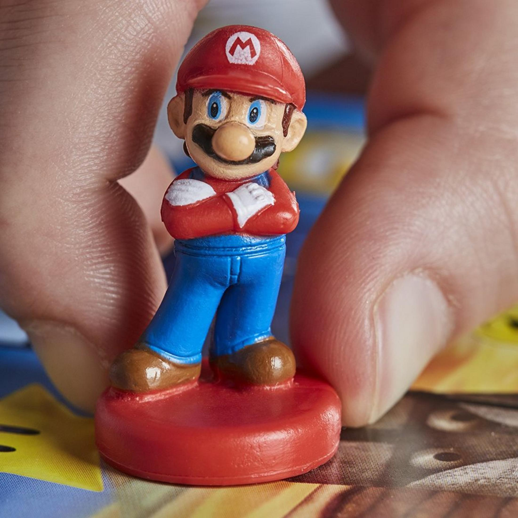 Eine Nahaufnahme zeigt eine Mario-Figur mit roter Mütze und blauer Latzhose, gehalten von zwei menschlichen Fingern.