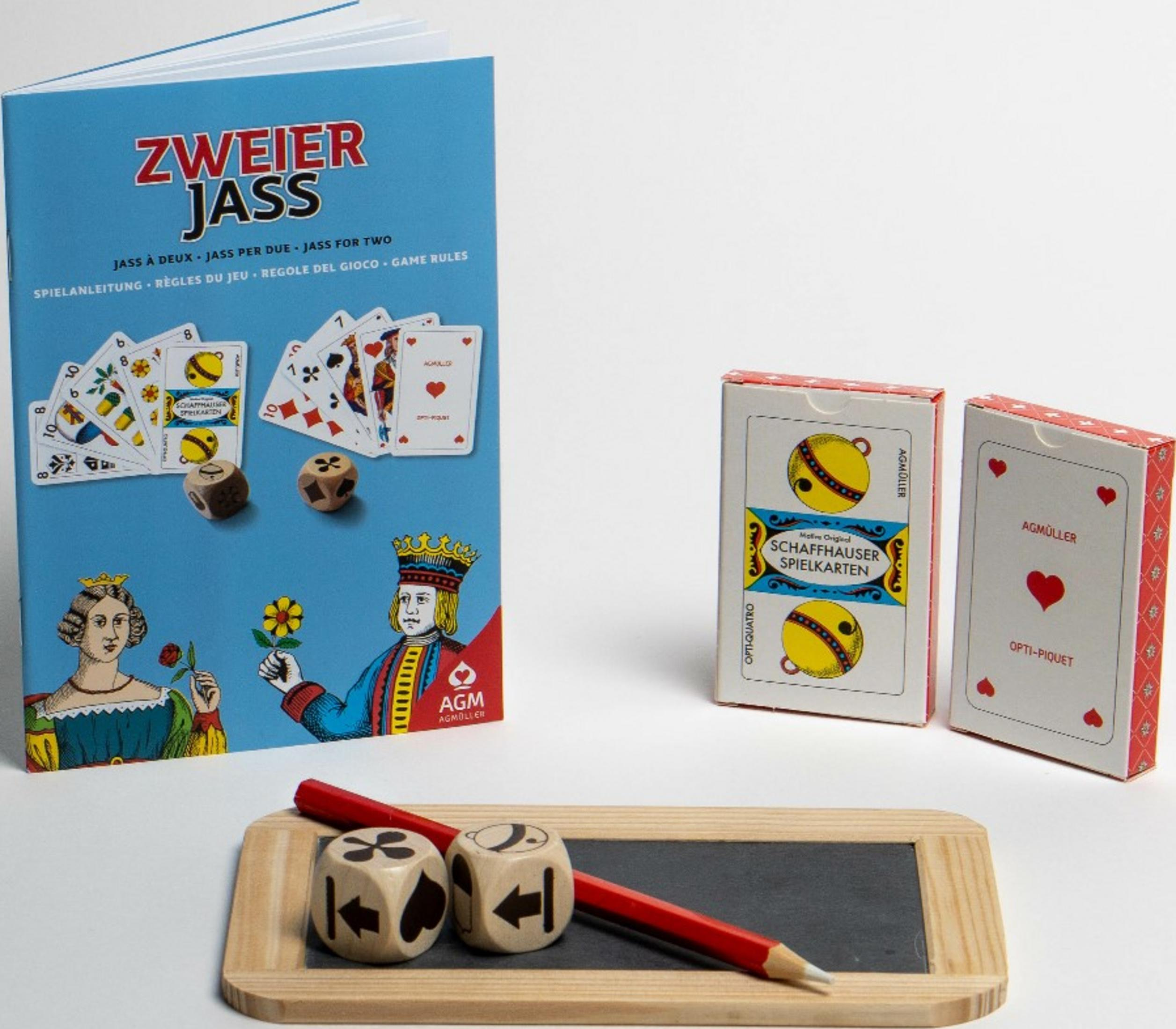 Ein blaues Kartenspiel-Regelbuch, zwei Kartendecks, zwei Würfel, ein roter Bleistift und eine kleine Tafel auf einer weißen Oberfläche.
