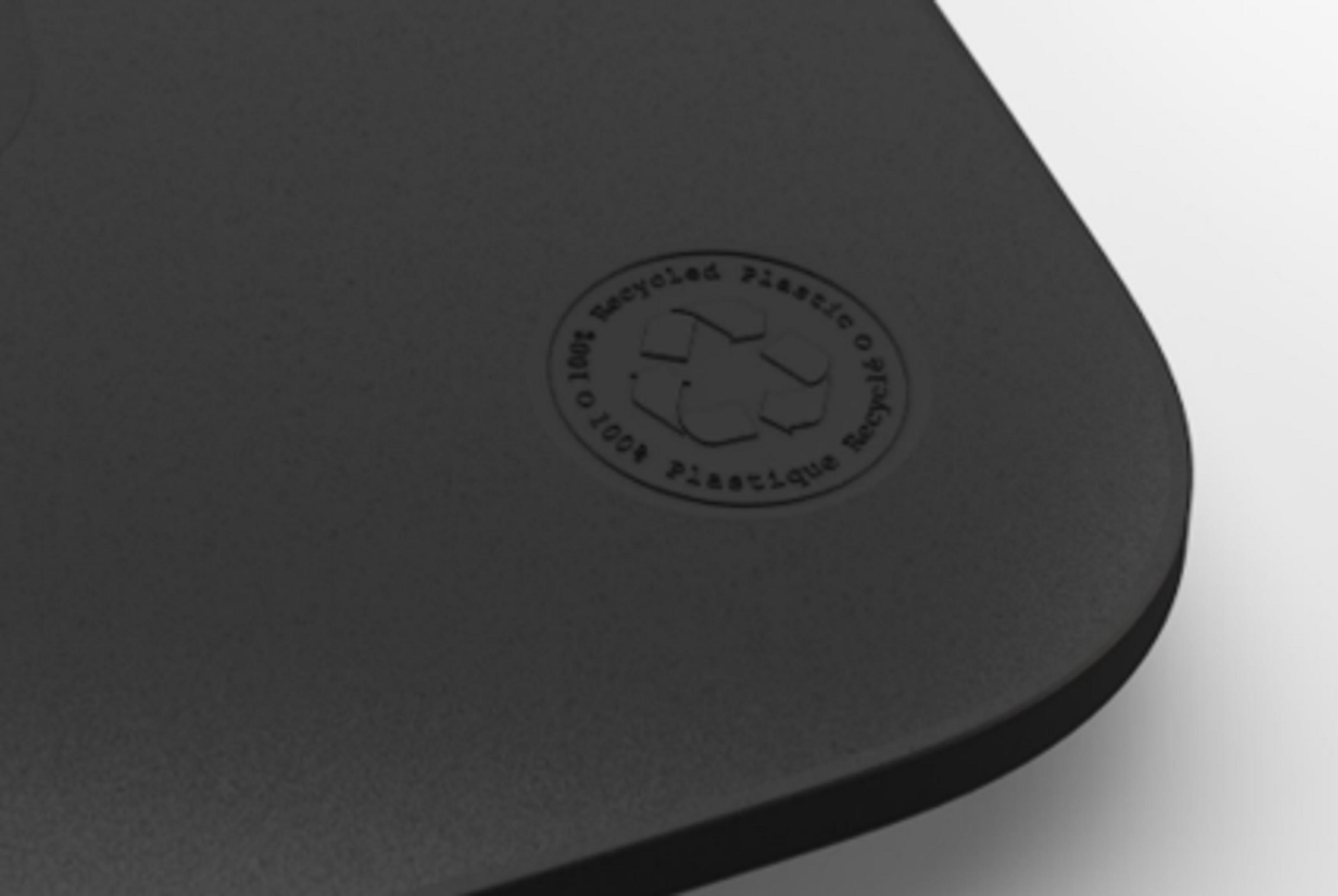 Zbliżenie ciemnoszarej teksturowanej powierzchni z delikatnym, wytłoczonym okrągłym logo recyklingu w górnym centrum.