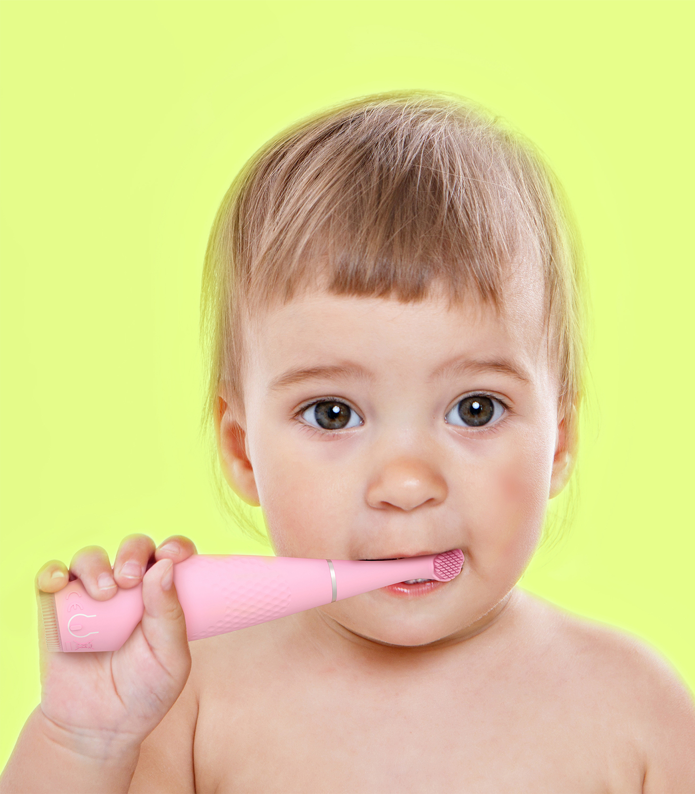 Un bambino con capelli castano chiaro e occhi scuri tiene uno spazzolino elettrico rosa alla bocca su uno sfondo verde lime.