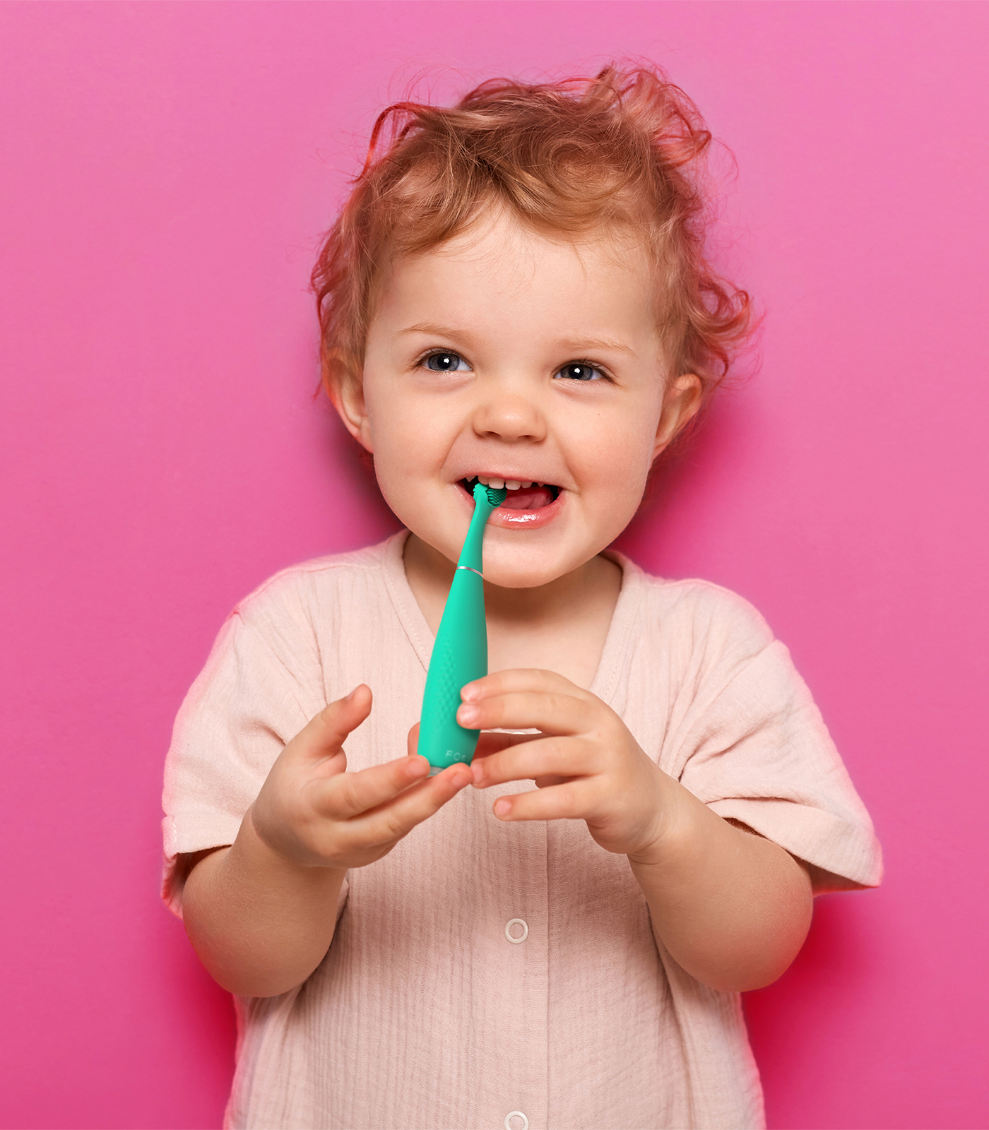 Un bimbo dai capelli ricci si lava i denti con uno spazzolino verde.