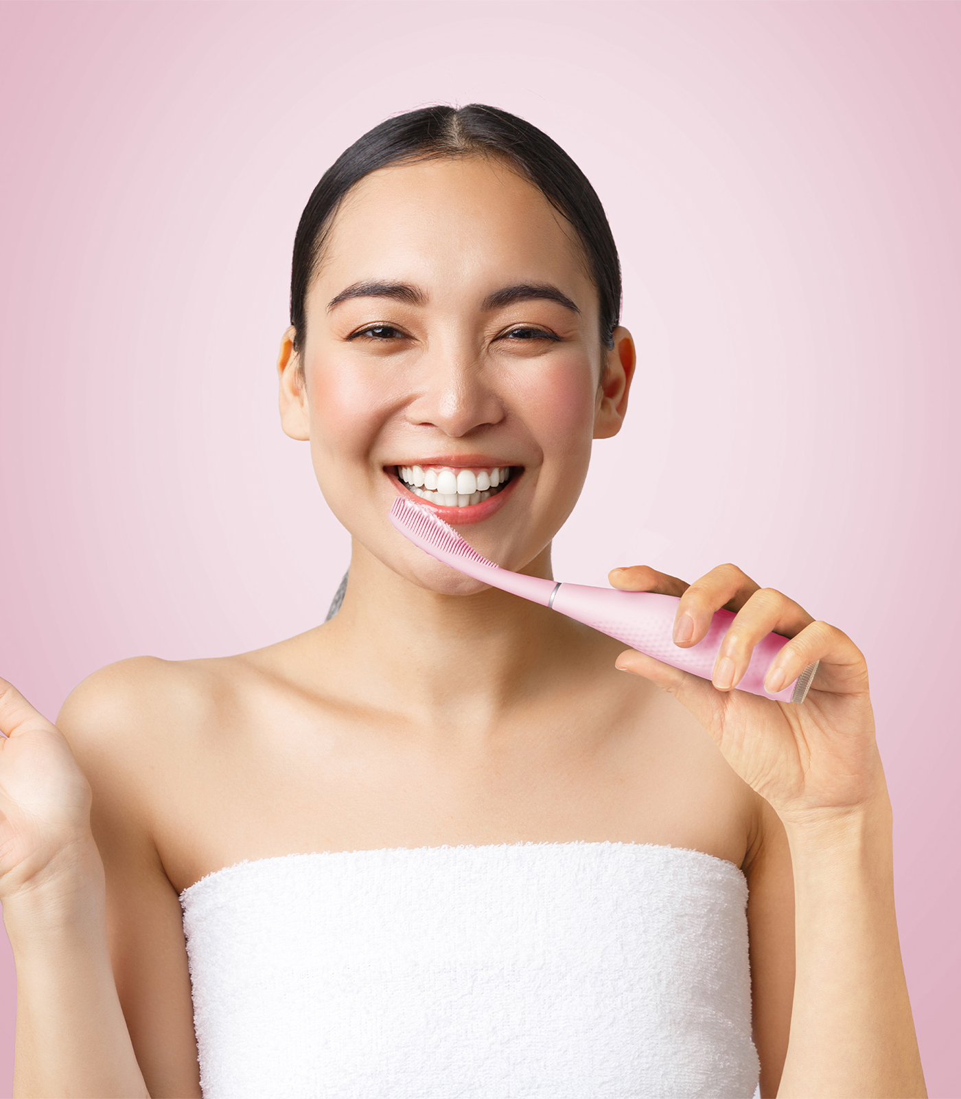 Una giovane donna con i capelli scuri raccolti, sorride luminosamente mentre tiene uno spazzolino elettrico rosa sui denti.