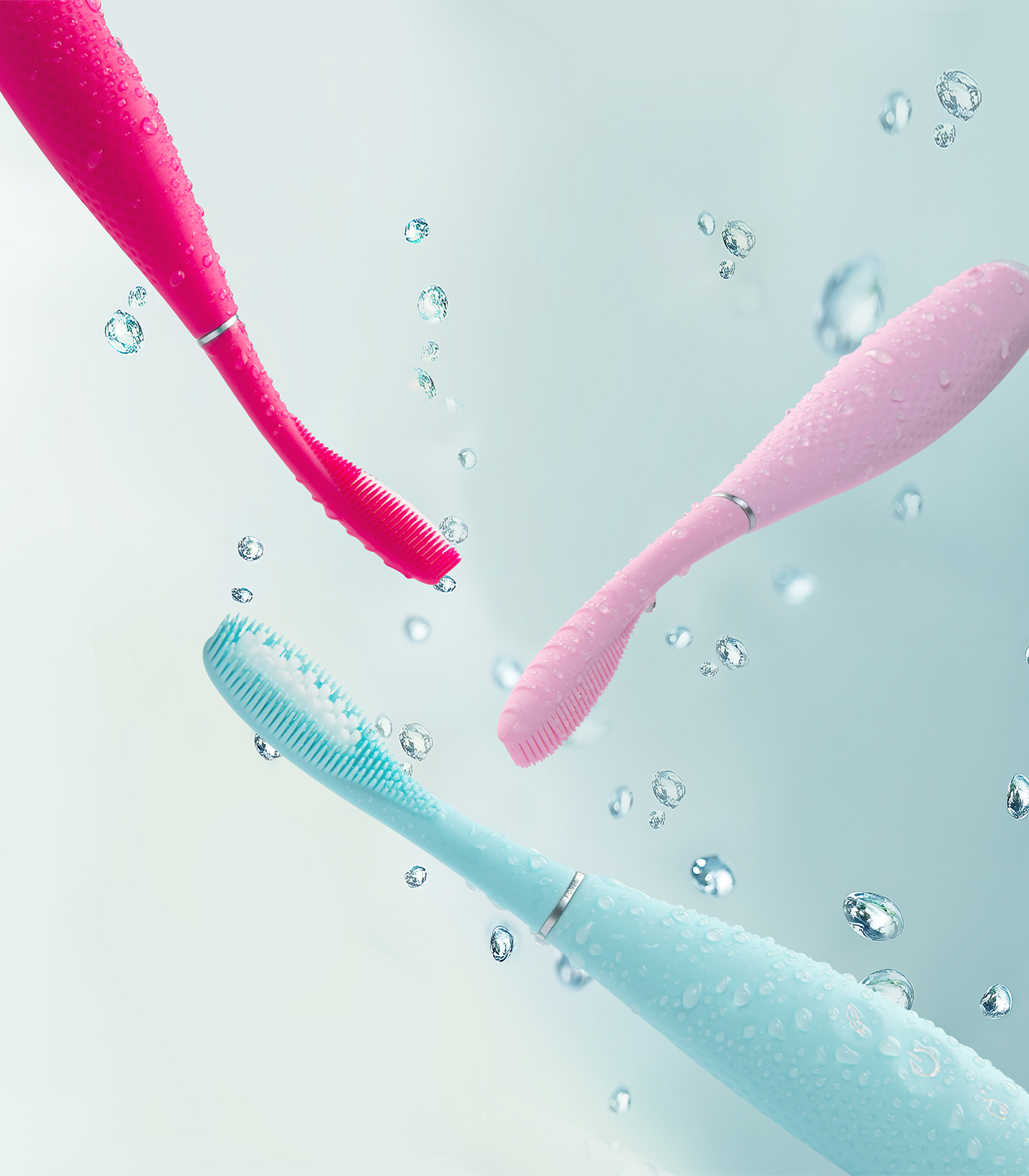 Tre spazzolini elettrici rosa, rosa e blu con gocce d'acqua.