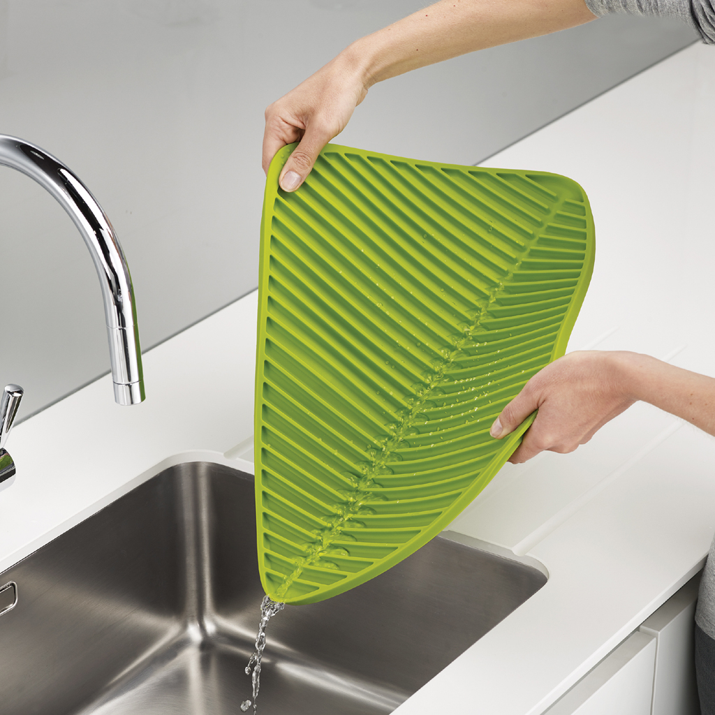 Tappetino scolapiatti verde a forma di foglia sopra il lavello, acqua che drena.